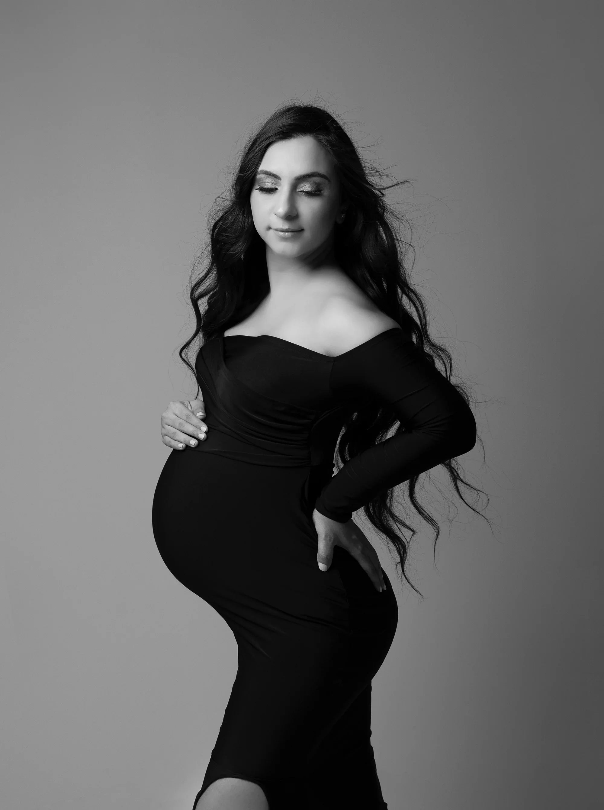 Pregnant woman in elegant off-shoulder black maternity gown posing confidently