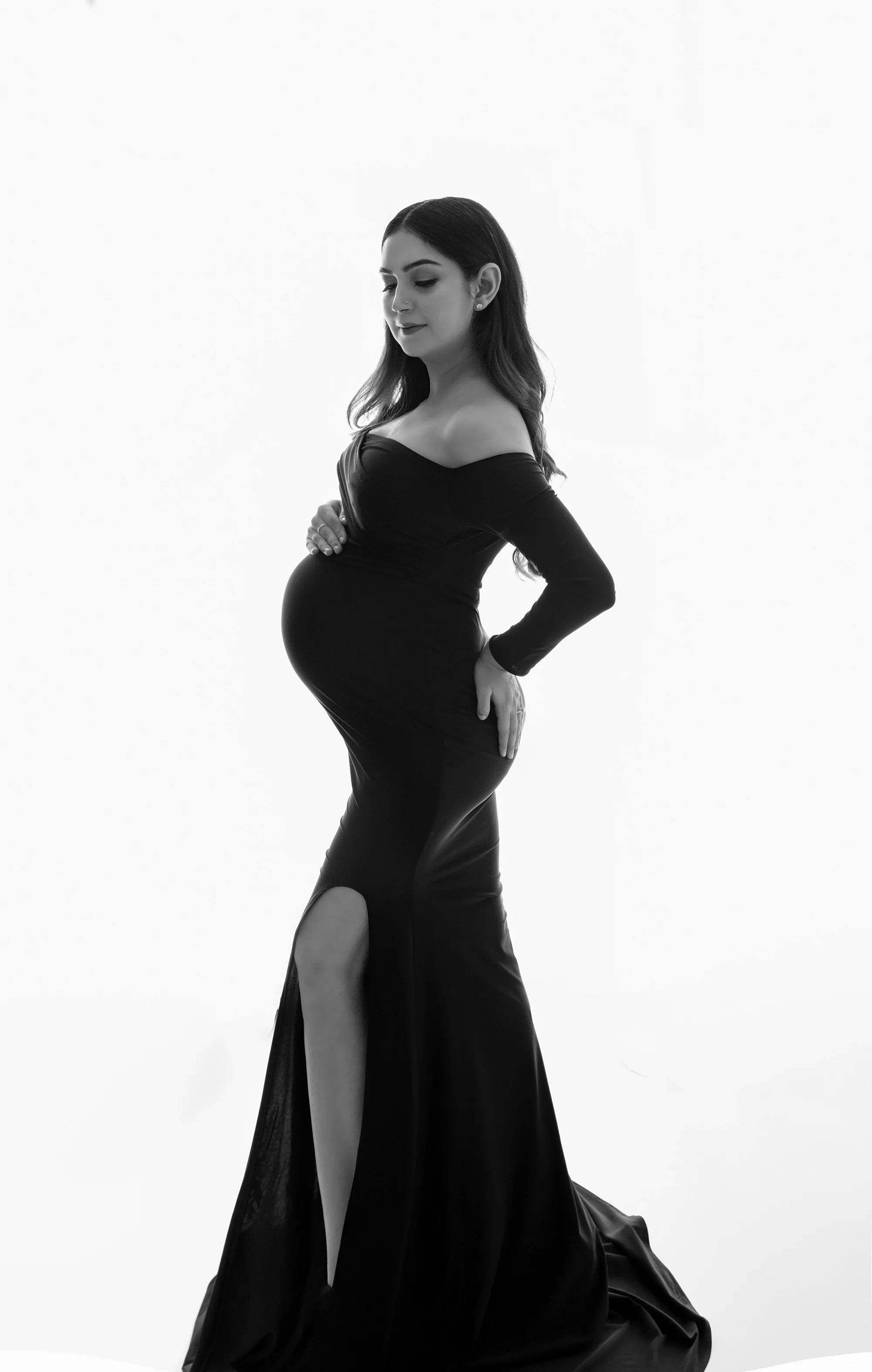 Pregnant woman in elegant off-shoulder maternity gown with front slit, studio portrait
