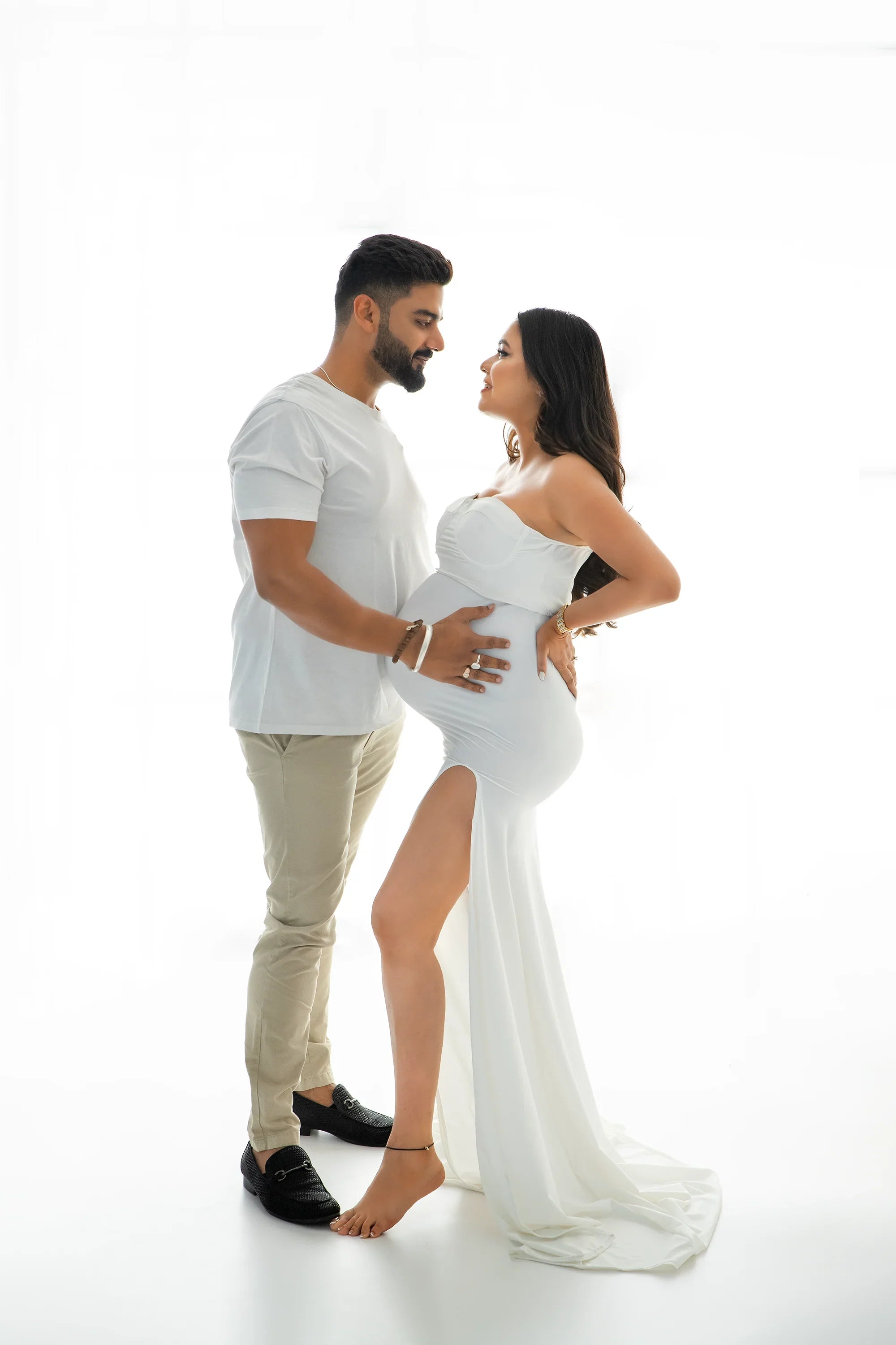 Pregnant woman in elegant white maternity gown with partner, studio portrait