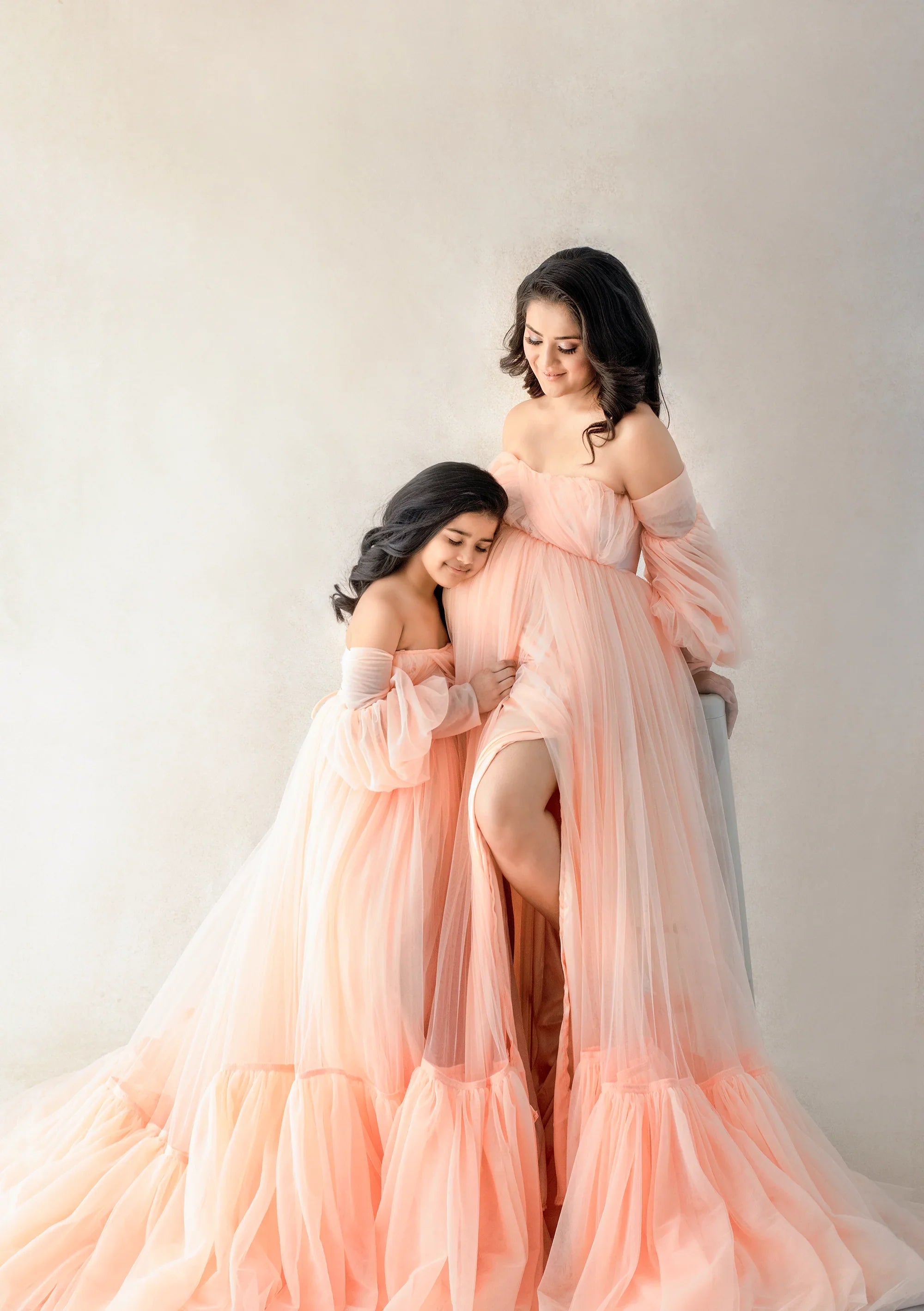 Mother and daughter in matching peach off-shoulder maternity gowns, elegant and stylish