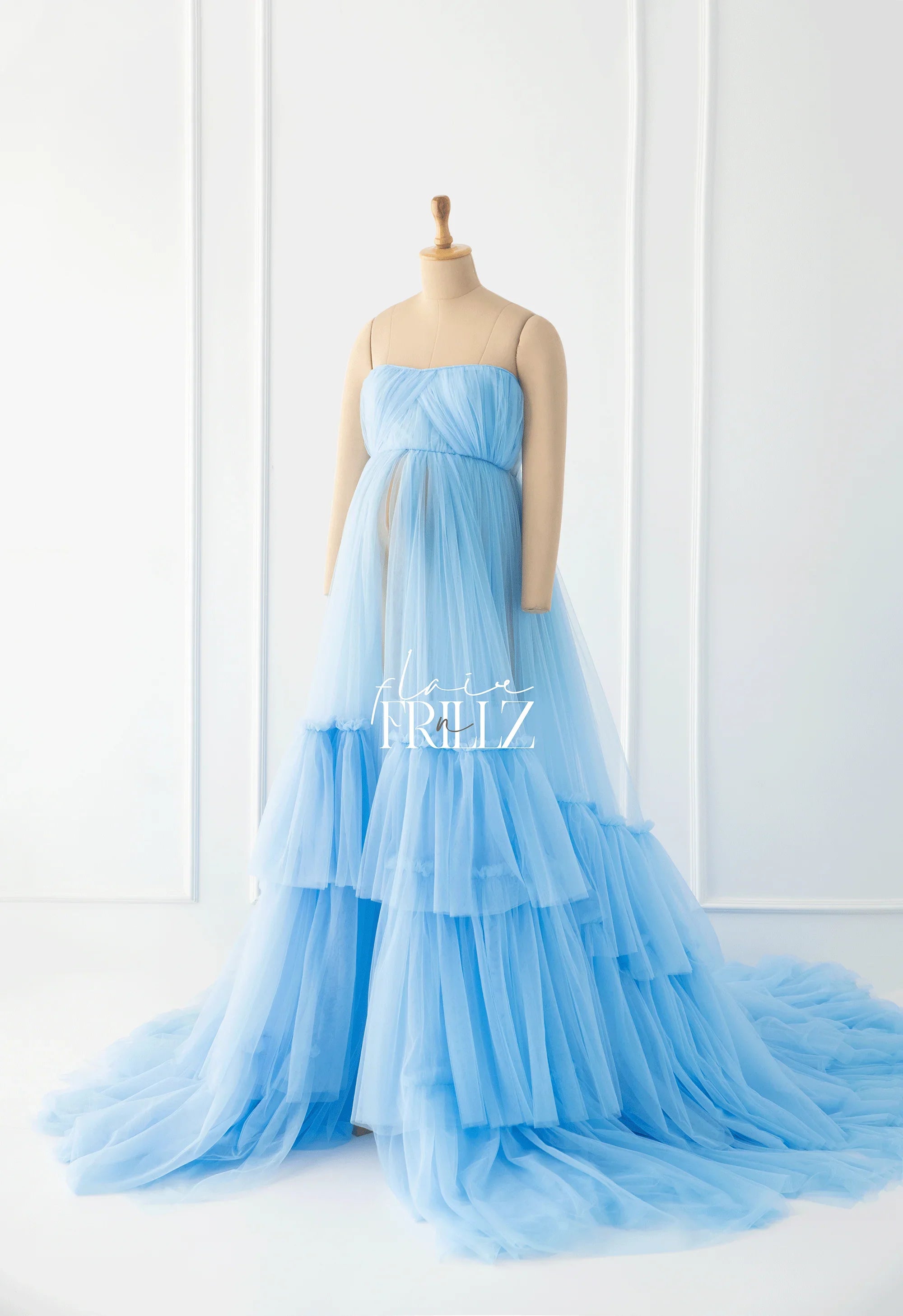 Light blue tulle maternity gown with tiered ruffles on a mannequin in a bright studio.