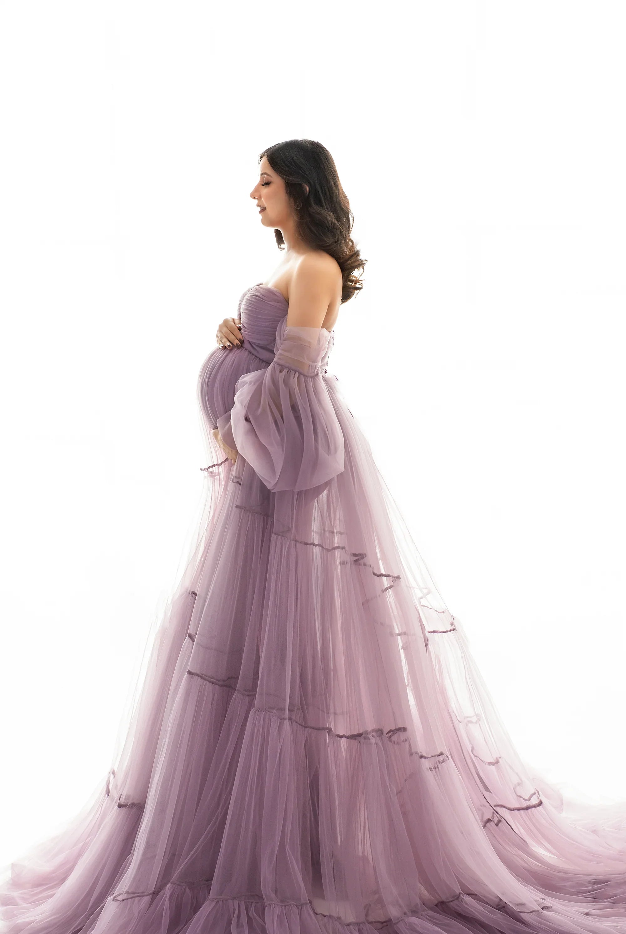 Pregnant woman in a flowing mauve maternity gown with puff sleeves, side profile
