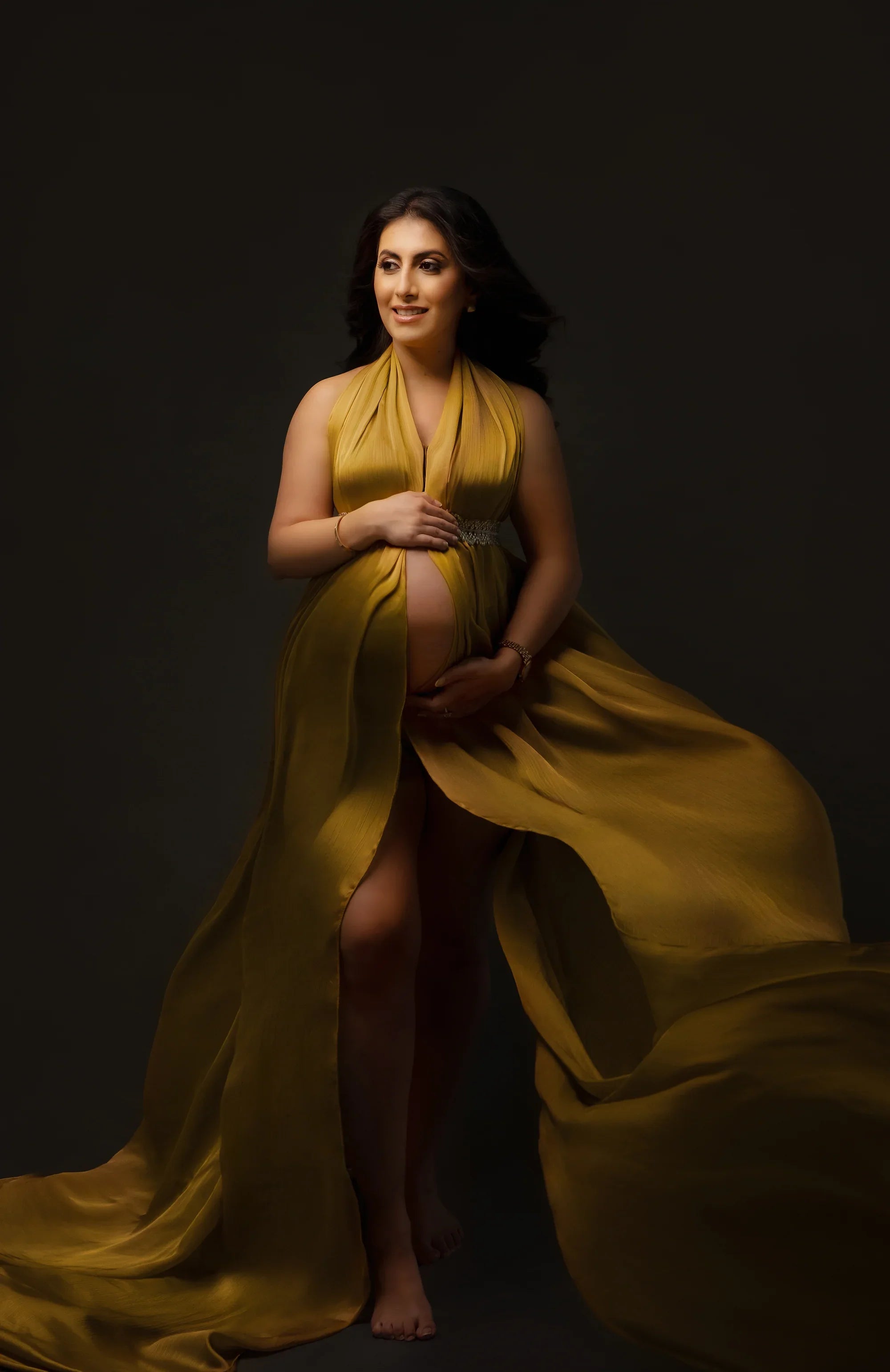 Pregnant woman in a flowing mustard yellow maternity gown posing confidently in studio