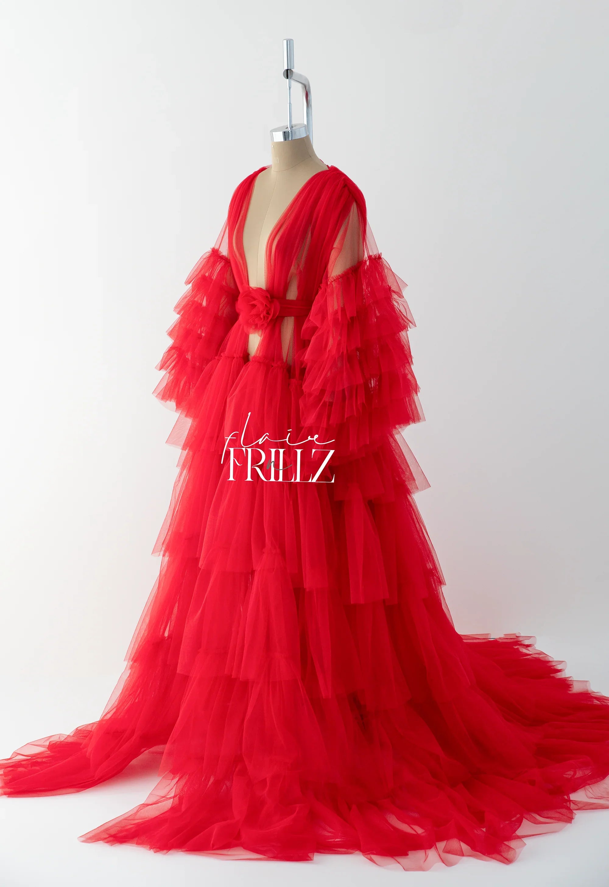 Vibrant red layered tulle maternity gown with deep V-neck and floral waist accent on mannequin