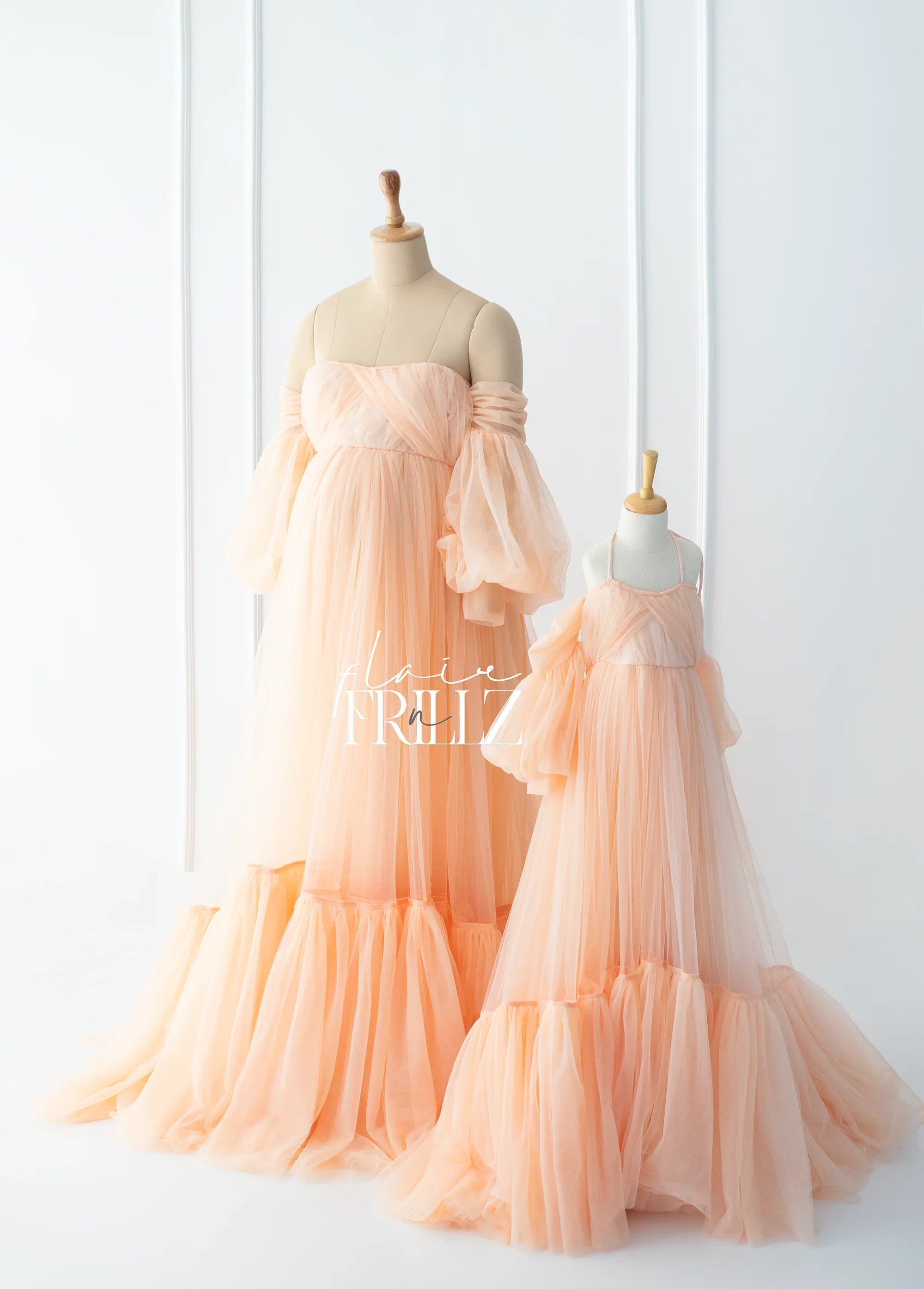 Peach tulle maternity gown and matching child dress on mannequins in a bright studio.