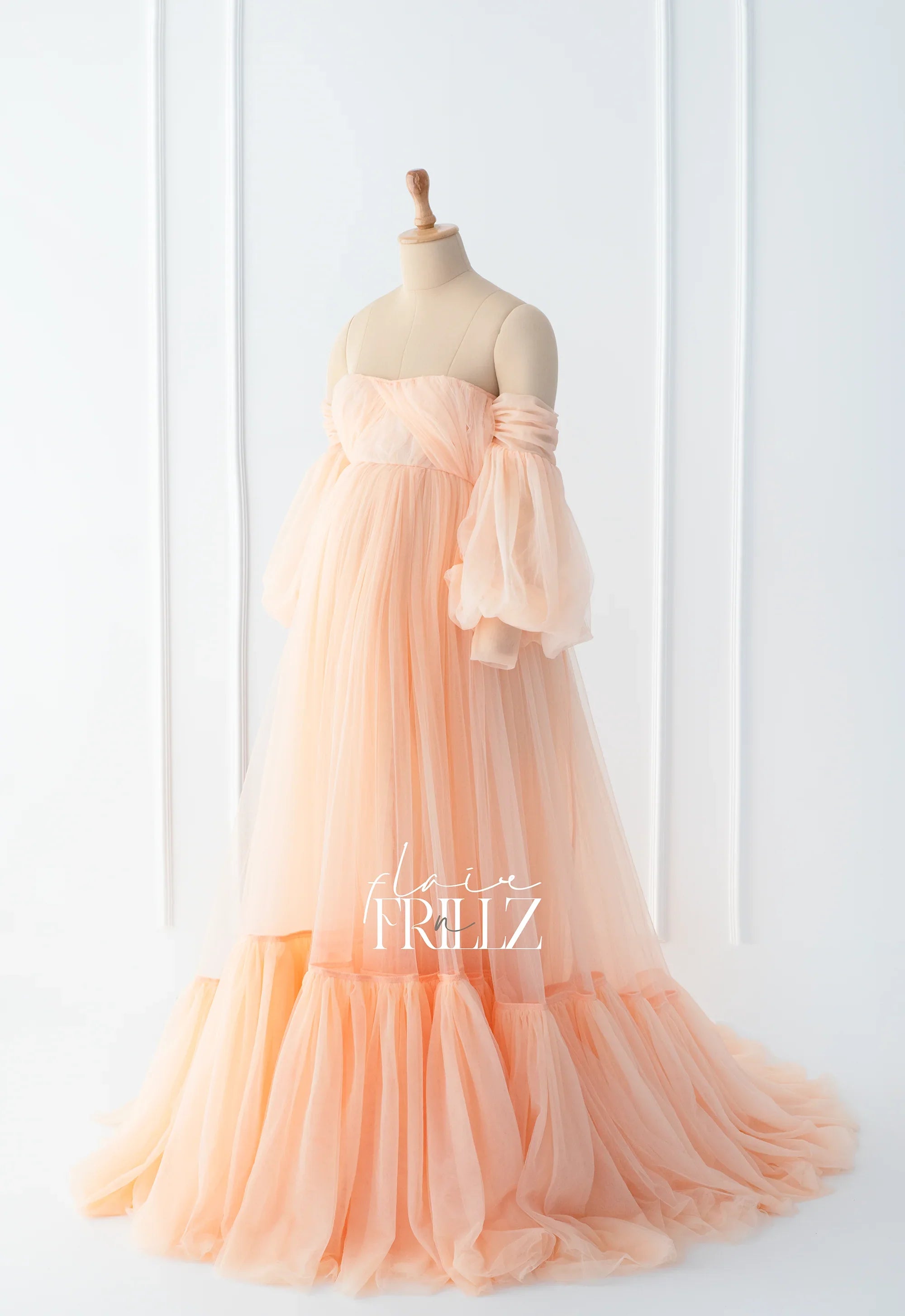 Peach tulle maternity gown with off-shoulder puff sleeves on dress form, elegant design