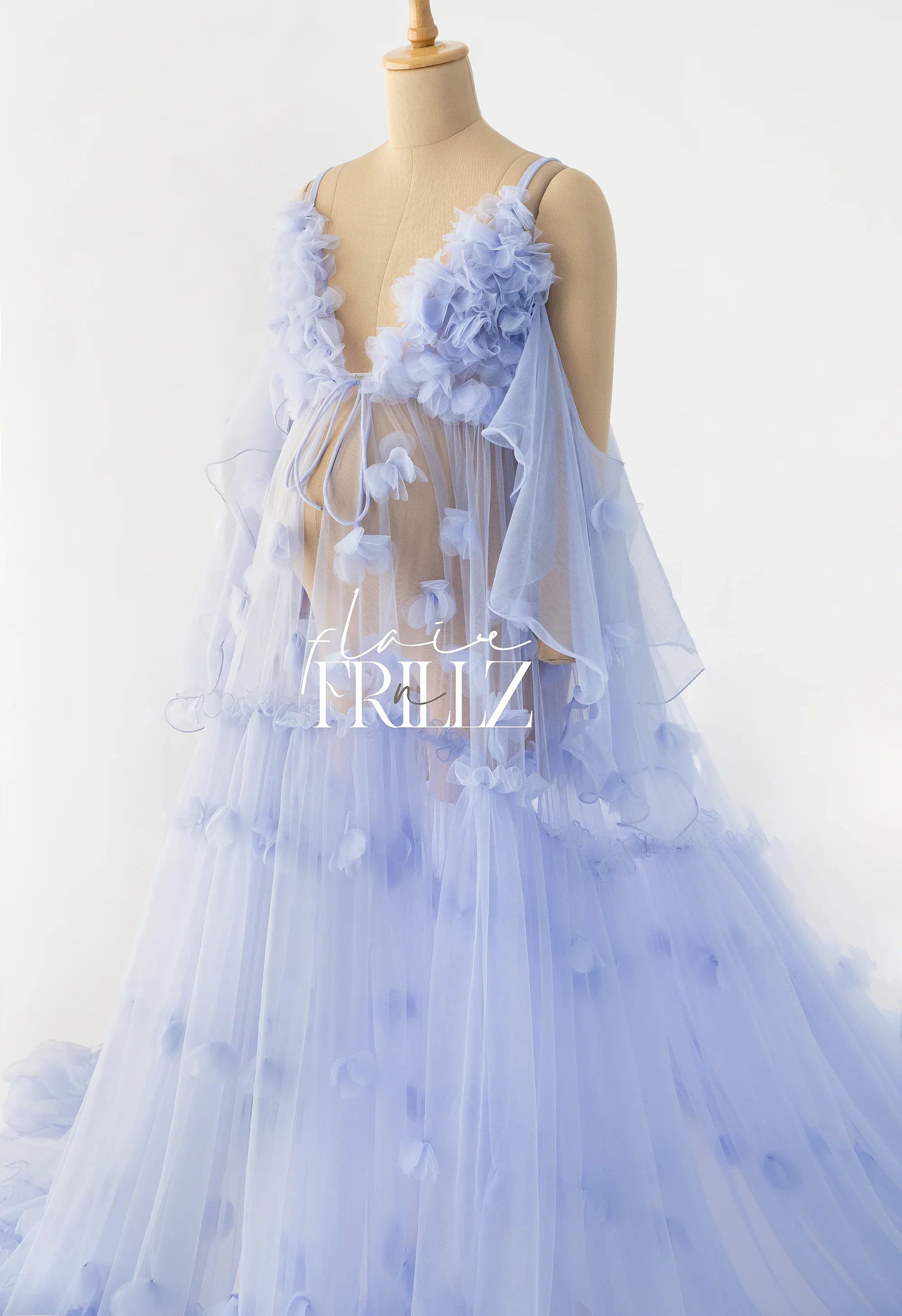 Pastel blue maternity gown with floral appliqué details and sheer tulle layers on mannequin