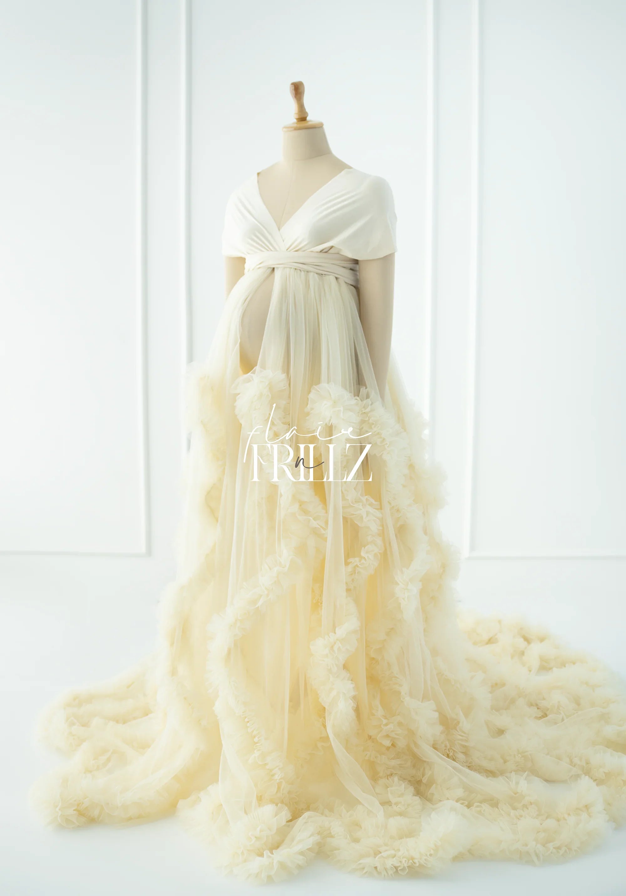Ivory maternity gown with sheer tulle overlay and ruffled trim on a mannequin