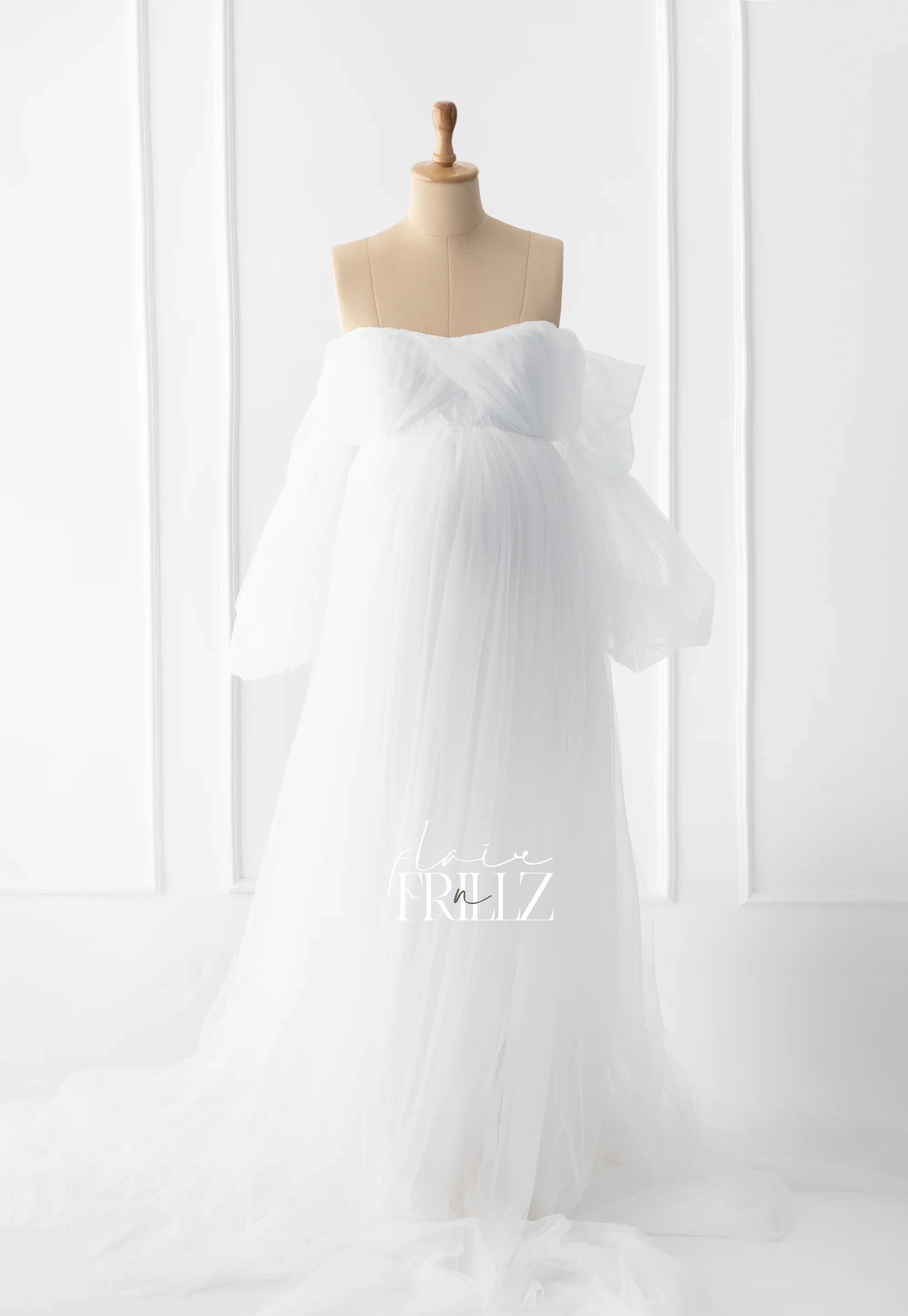 White off-shoulder tulle maternity gown on mannequin in bright, elegant studio setting
