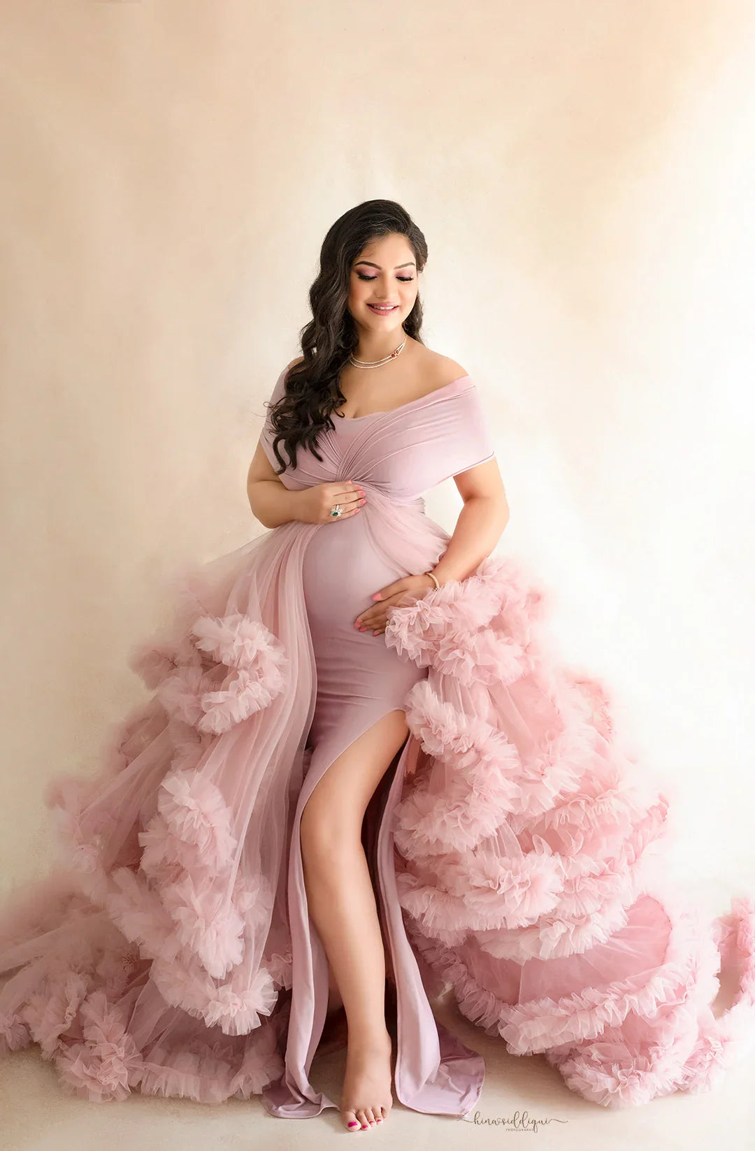Pregnant woman in elegant pink off-shoulder maternity gown with ruffled tulle layers
