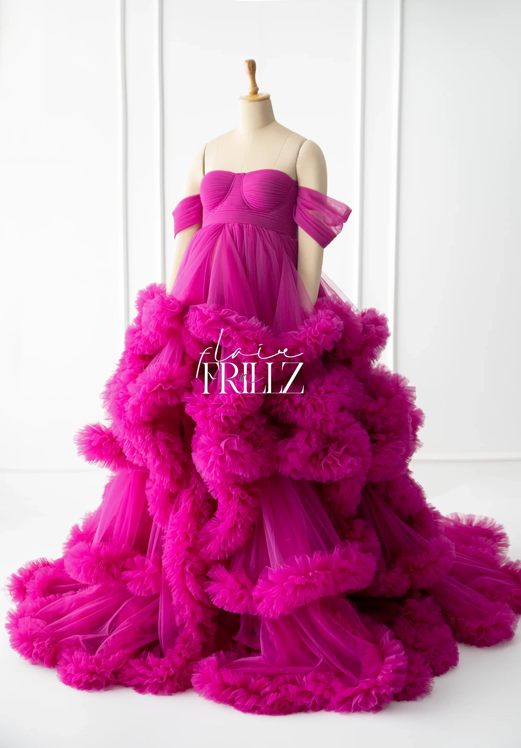 Vibrant fuchsia maternity gown with ruffled tulle layers and off-shoulder sleeves on mannequin