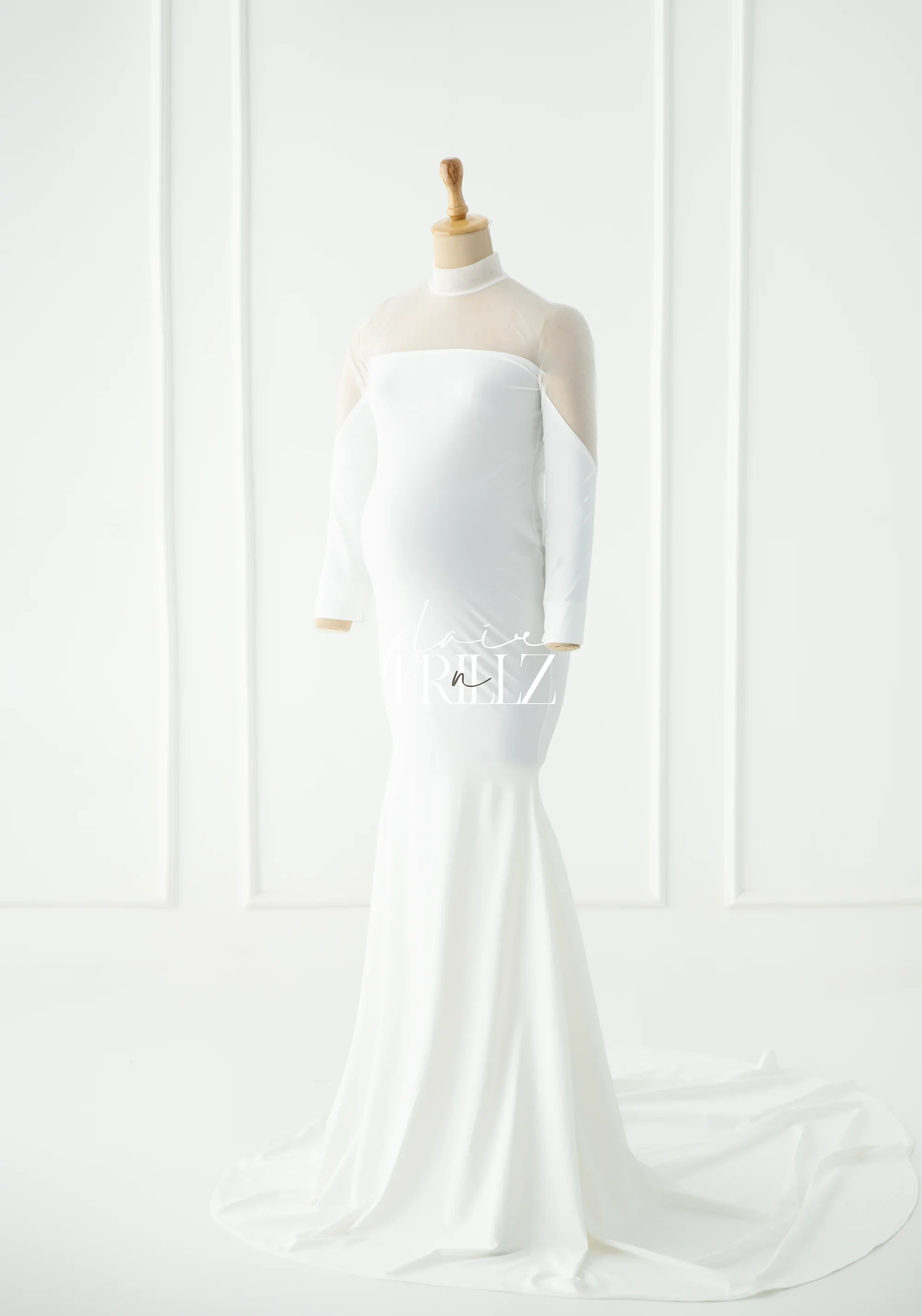 Elegant white maternity gown with sheer long sleeves on a mannequin in a bright studio