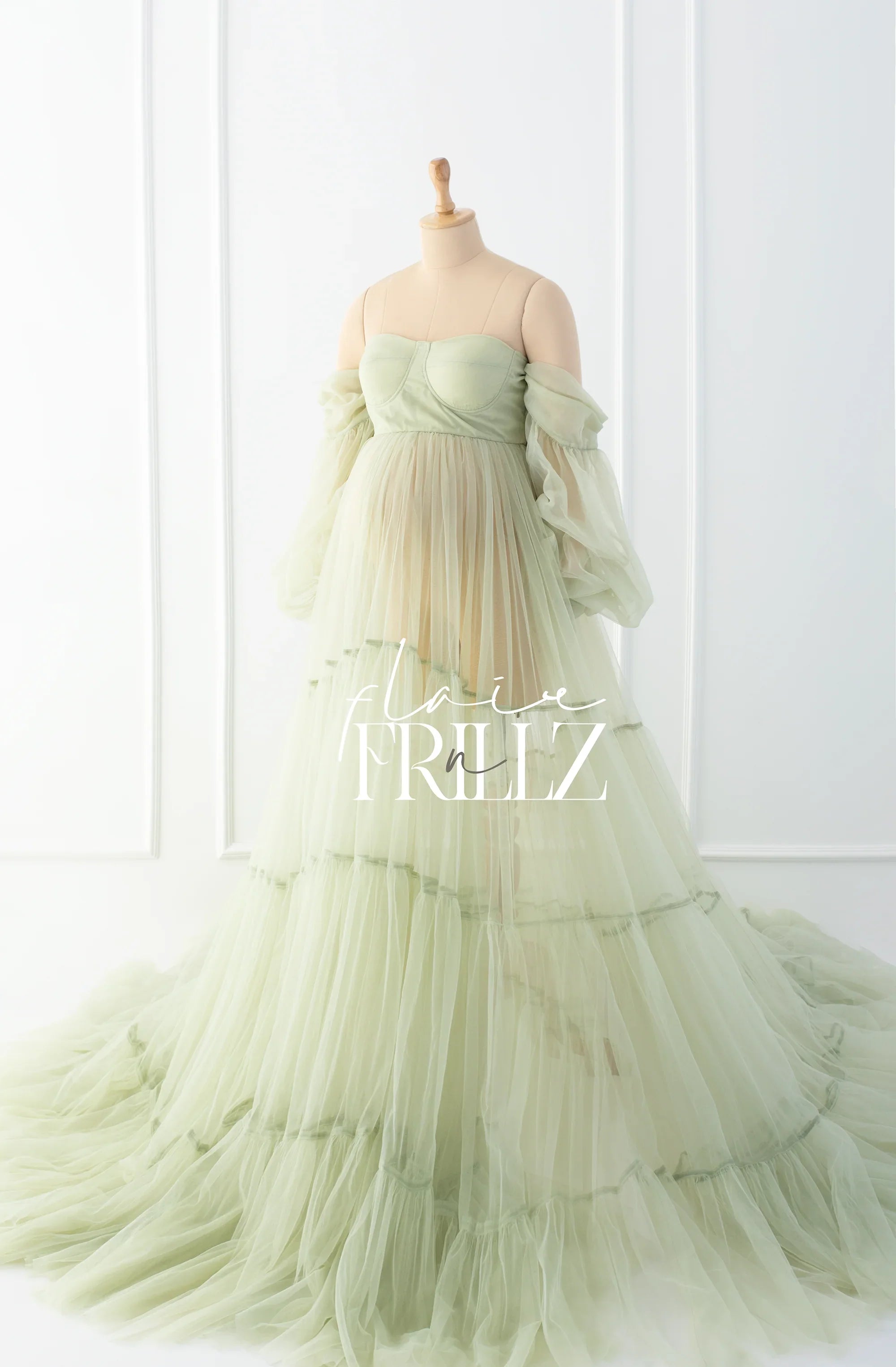 Sage green maternity gown with off-shoulder tulle sleeves and layered flowing skirt on mannequin