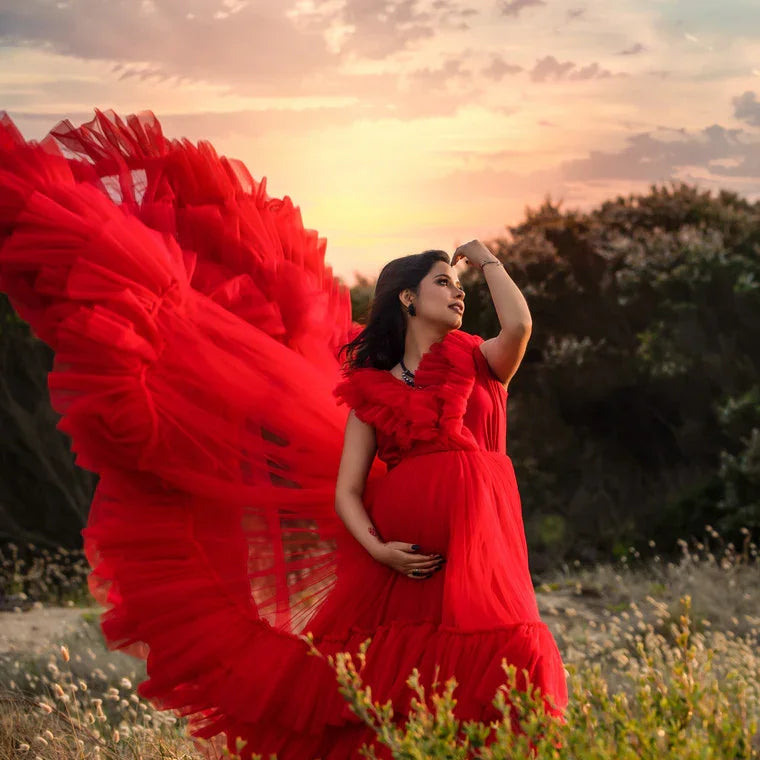 Pregnant woman in a flowing red maternity gown posing outdoors at sunset