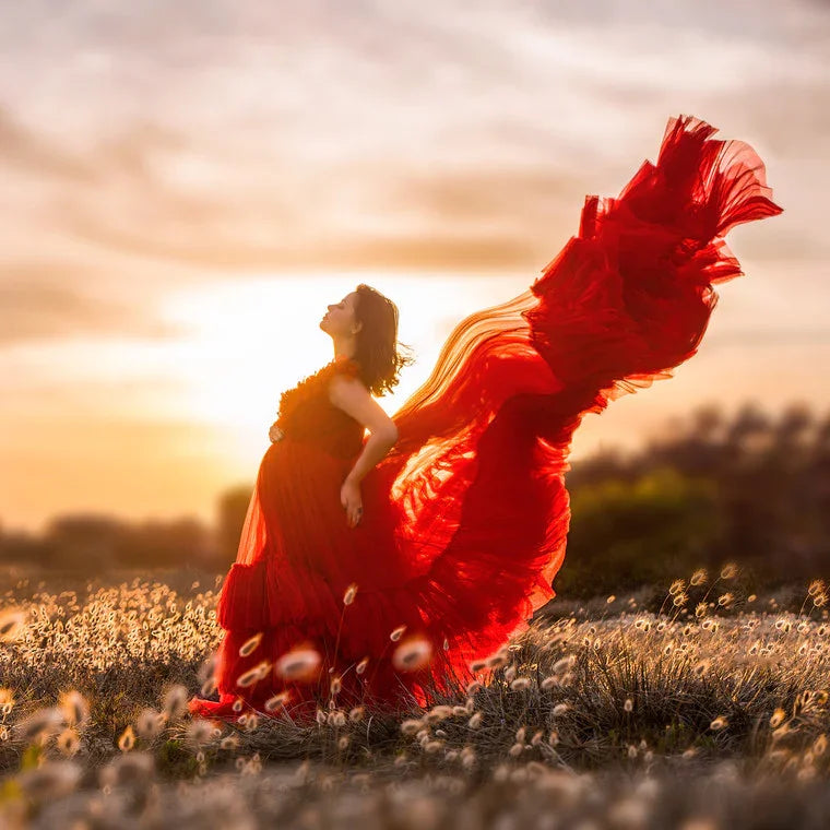 Pregnant woman in flowing red maternity gown posing outdoors at sunset in a field