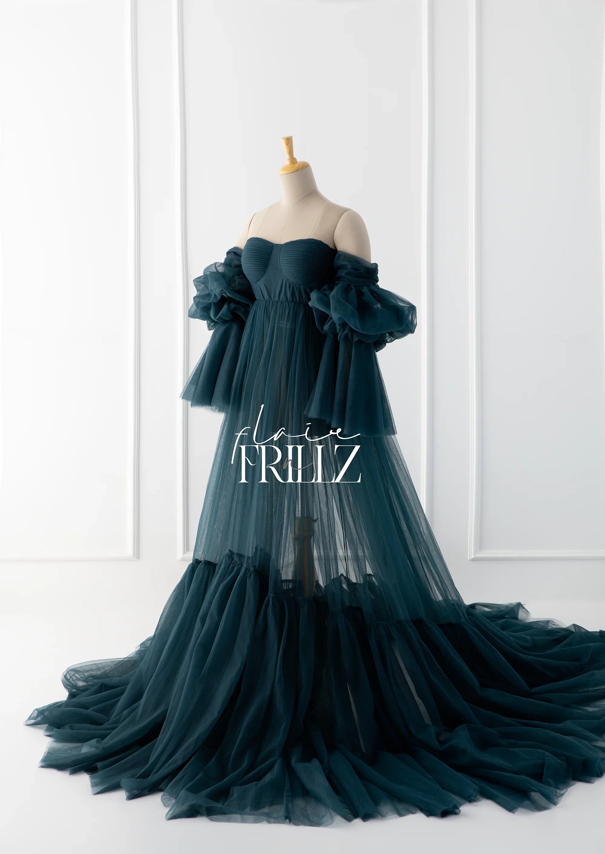 Sheer dark teal maternity gown with off-shoulder ruffled sleeves on a mannequin