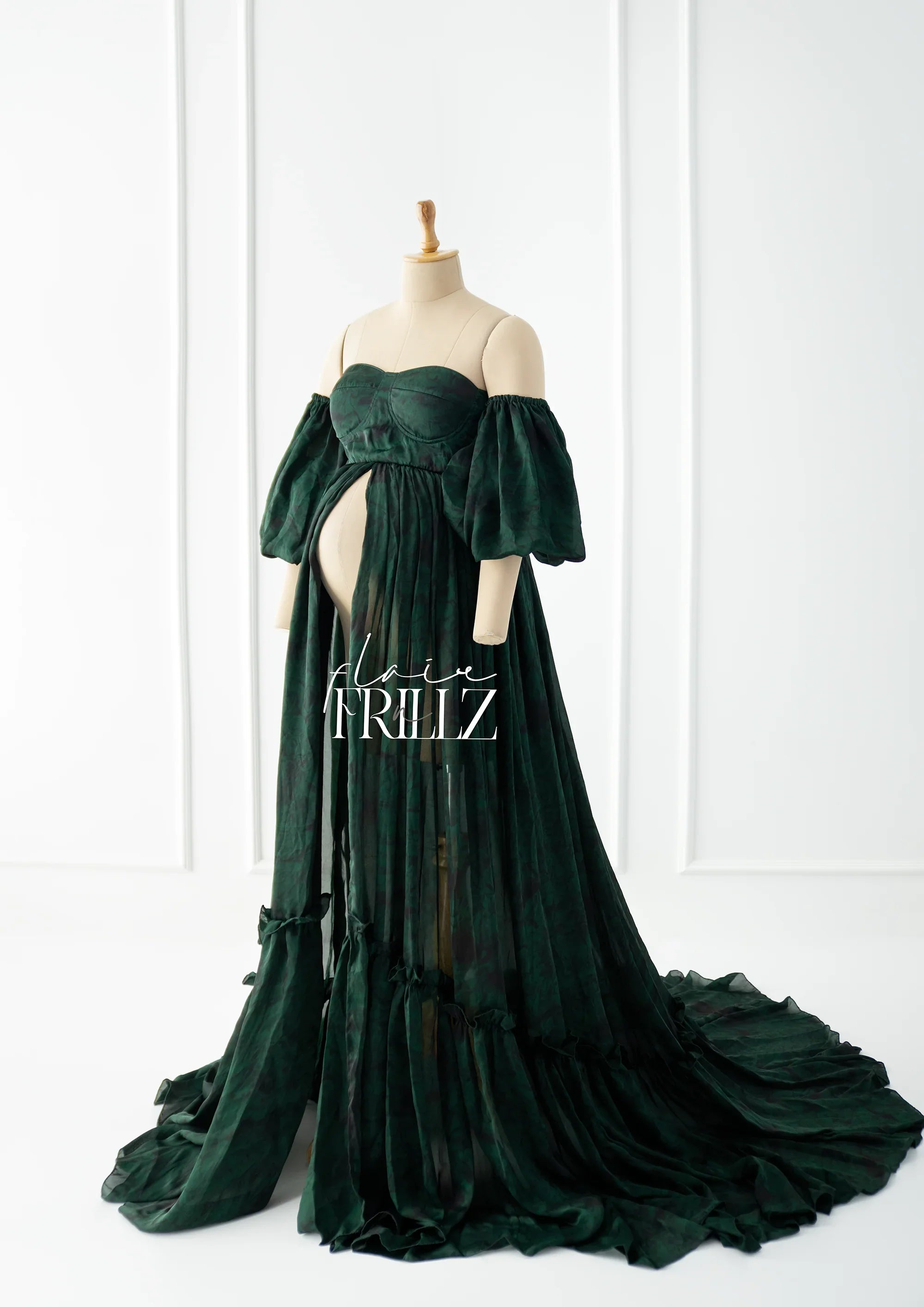 Dark green off-shoulder maternity gown with puff sleeves and flowing sheer train on a mannequin