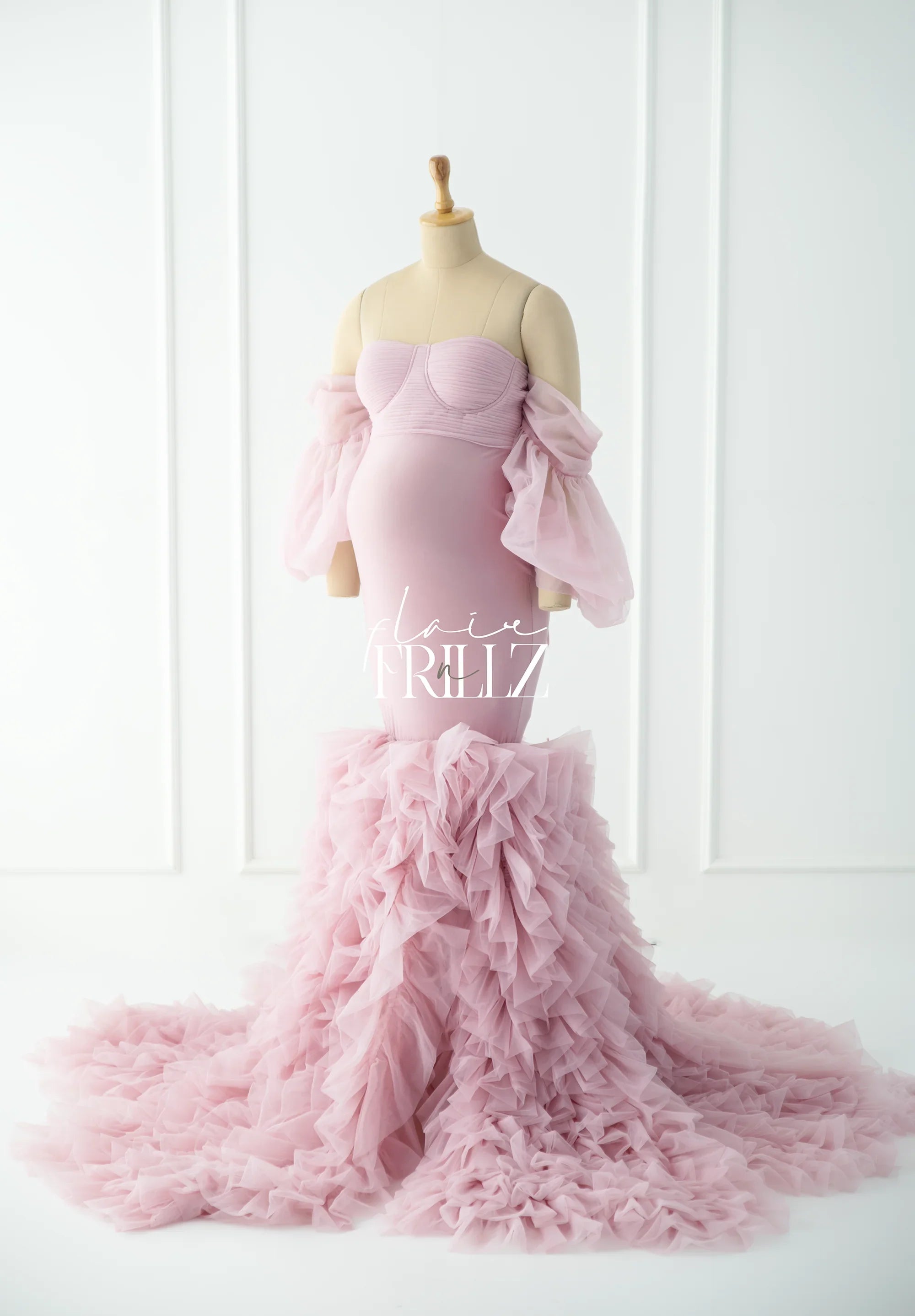 Light pink ruffled maternity gown with off-shoulder sleeves displayed on mannequin