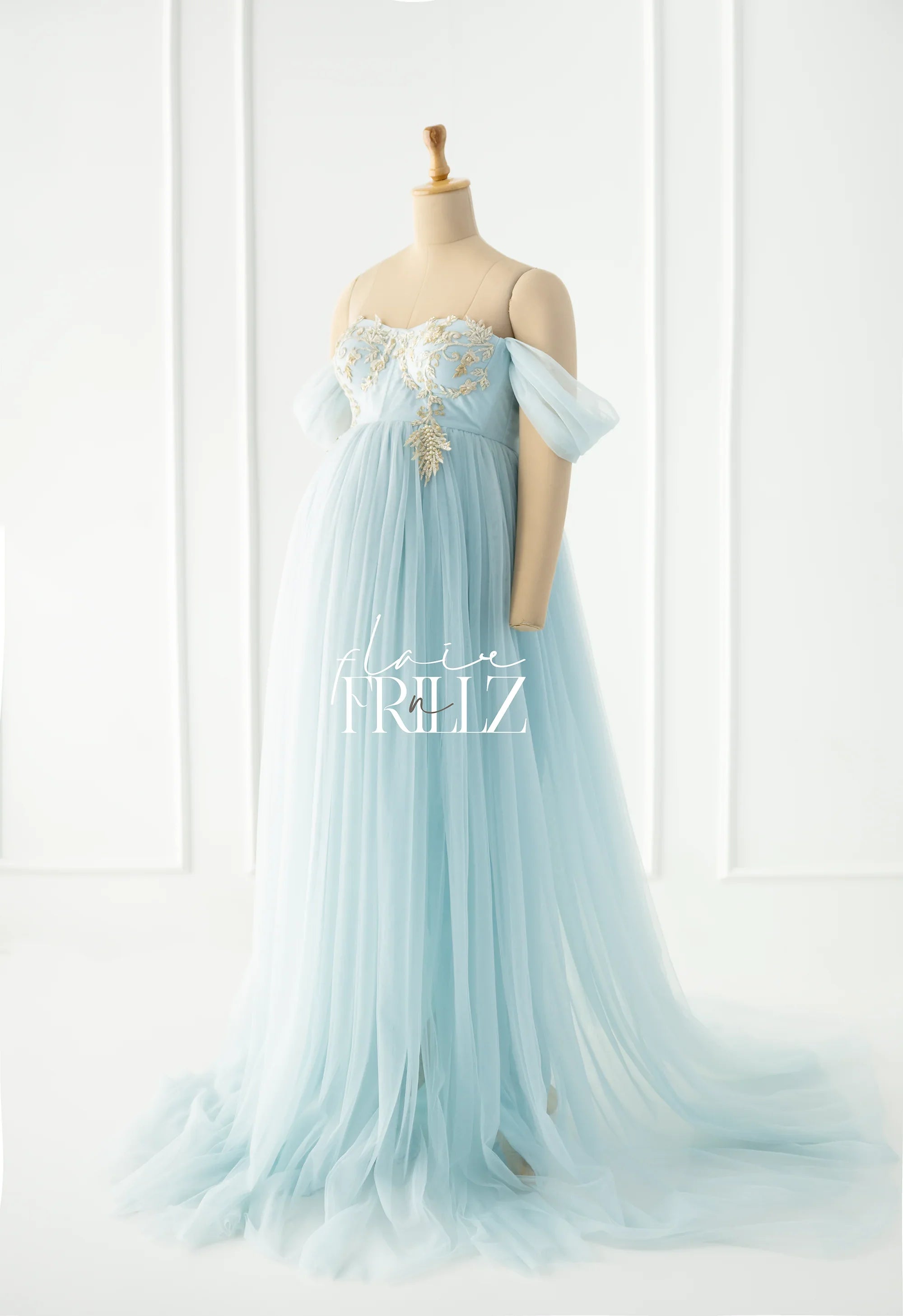 Light blue off-shoulder maternity gown with gold embroidery on a mannequin, flowing tulle skirt