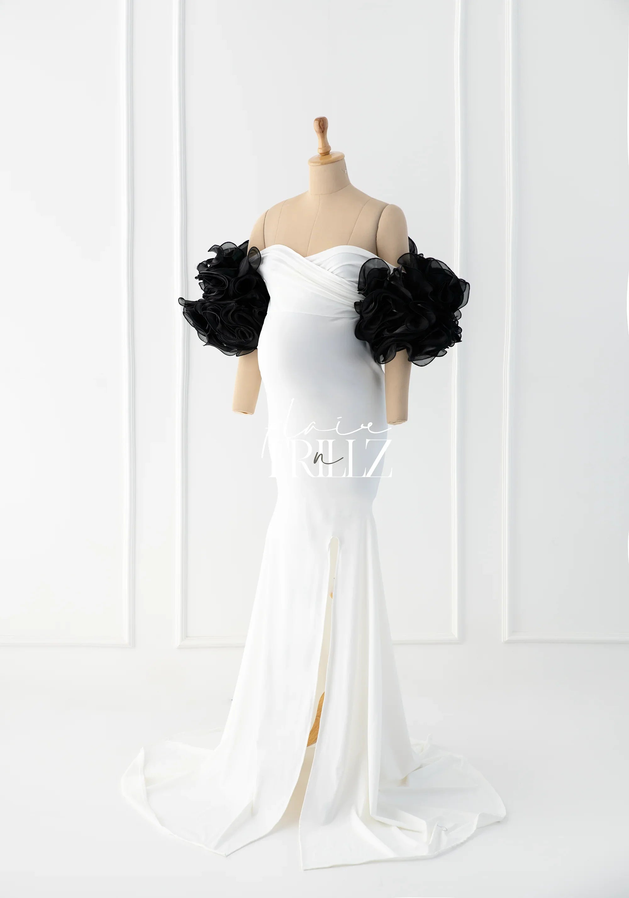 Elegant white maternity gown with dramatic black ruffled sleeves on mannequin