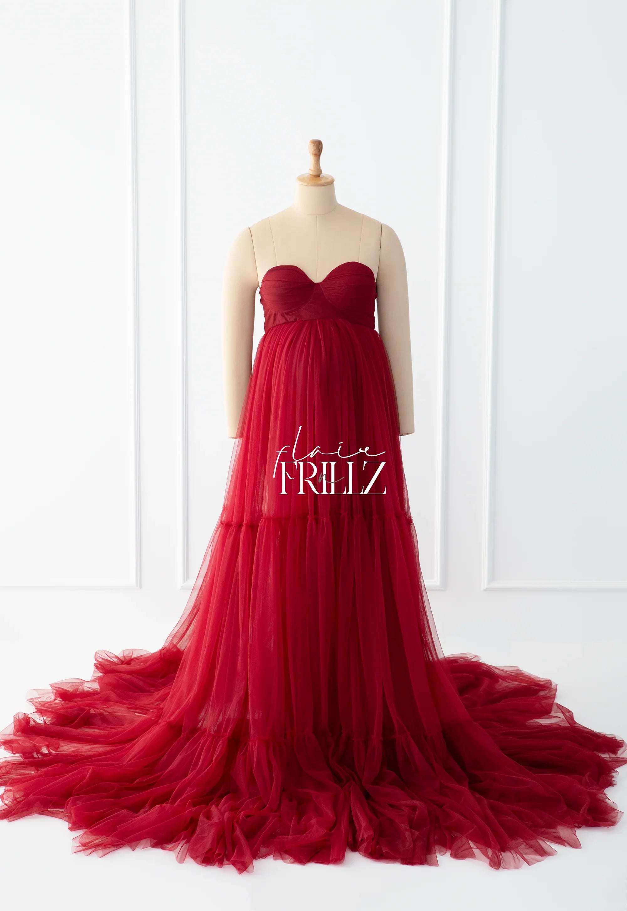 Elegant strapless red maternity gown with flowing tulle train on mannequin