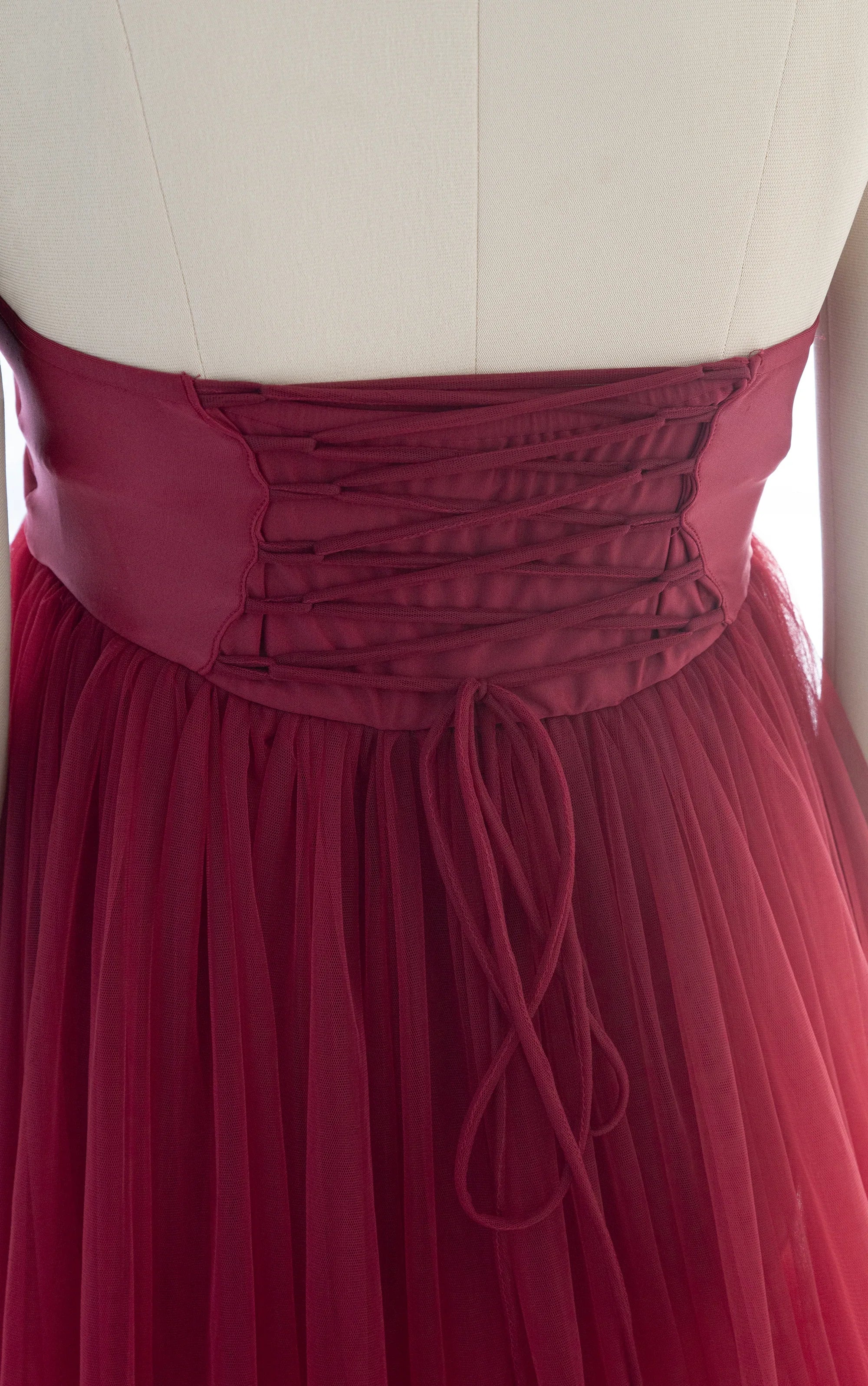 Back view of a burgundy maternity gown with lace-up corset and tulle skirt details