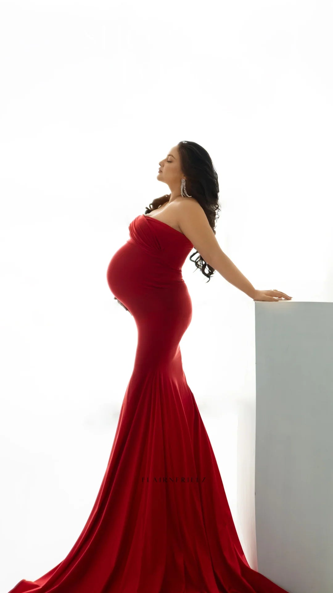 Pregnant woman in flowing red maternity gown posing elegantly against a white background