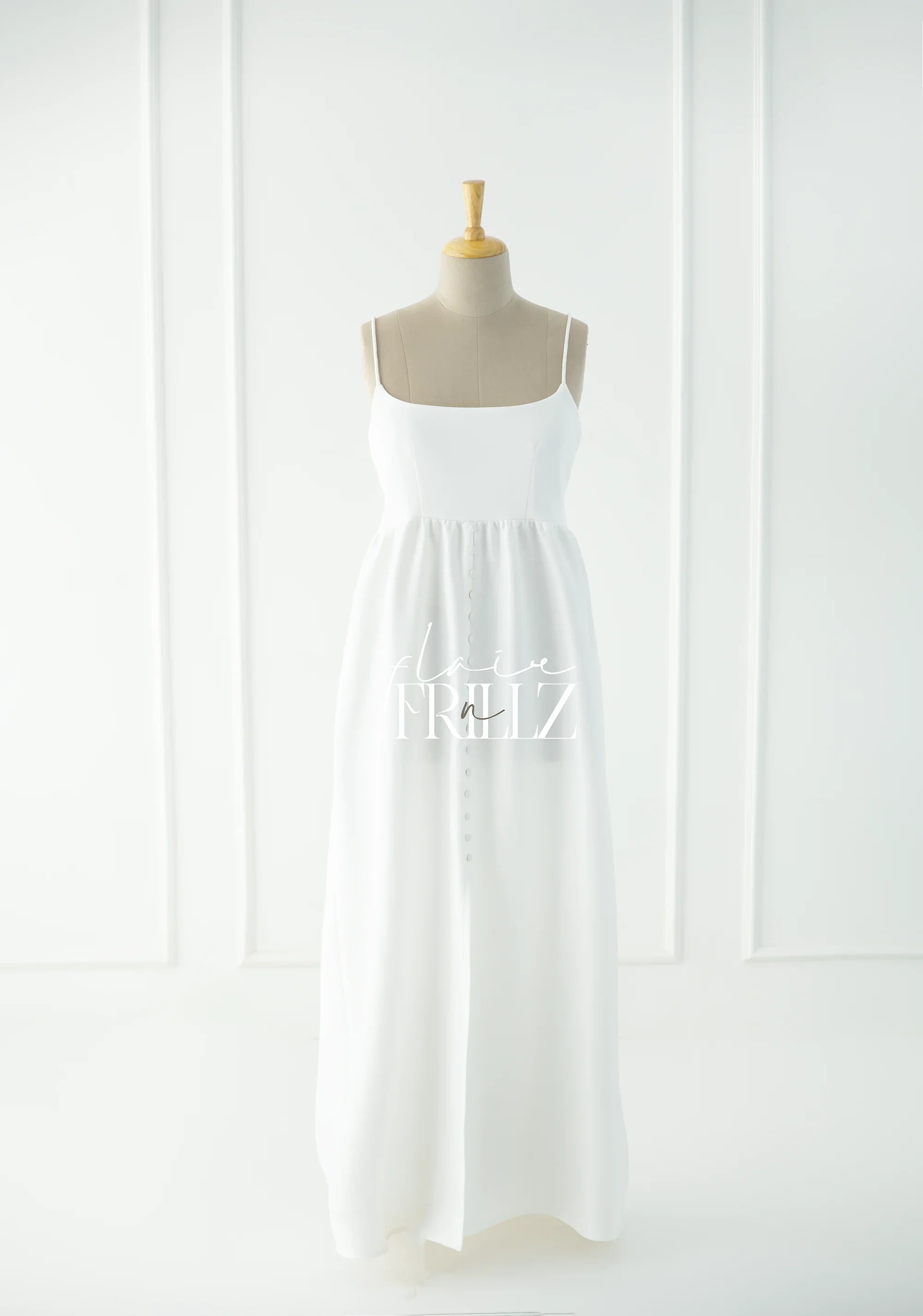 Elegant white maternity gown with spaghetti straps and button details on mannequin