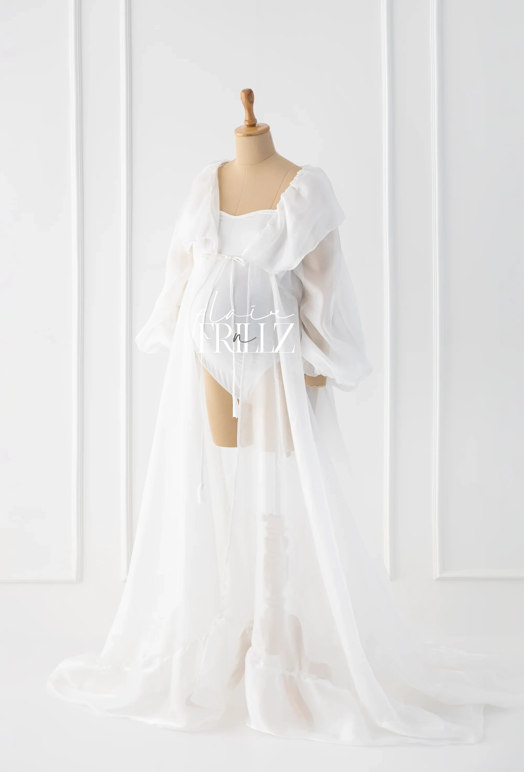 Sheer white maternity gown with long sleeves and flowing train on dress form