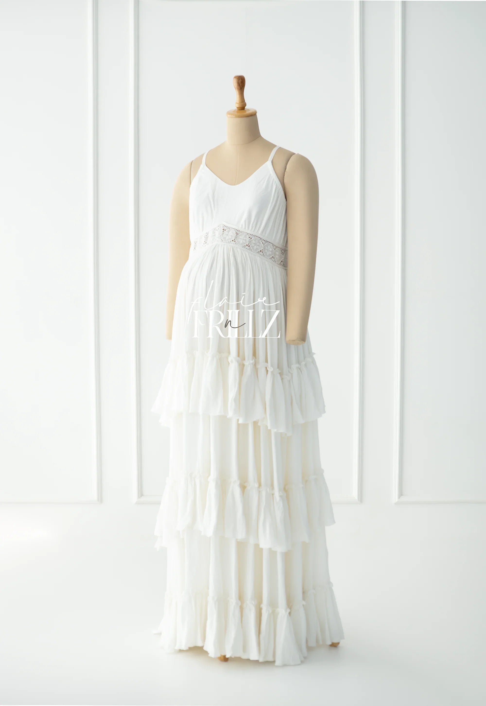 White boho tiered maternity gown with lace trim displayed on mannequin in bright studio