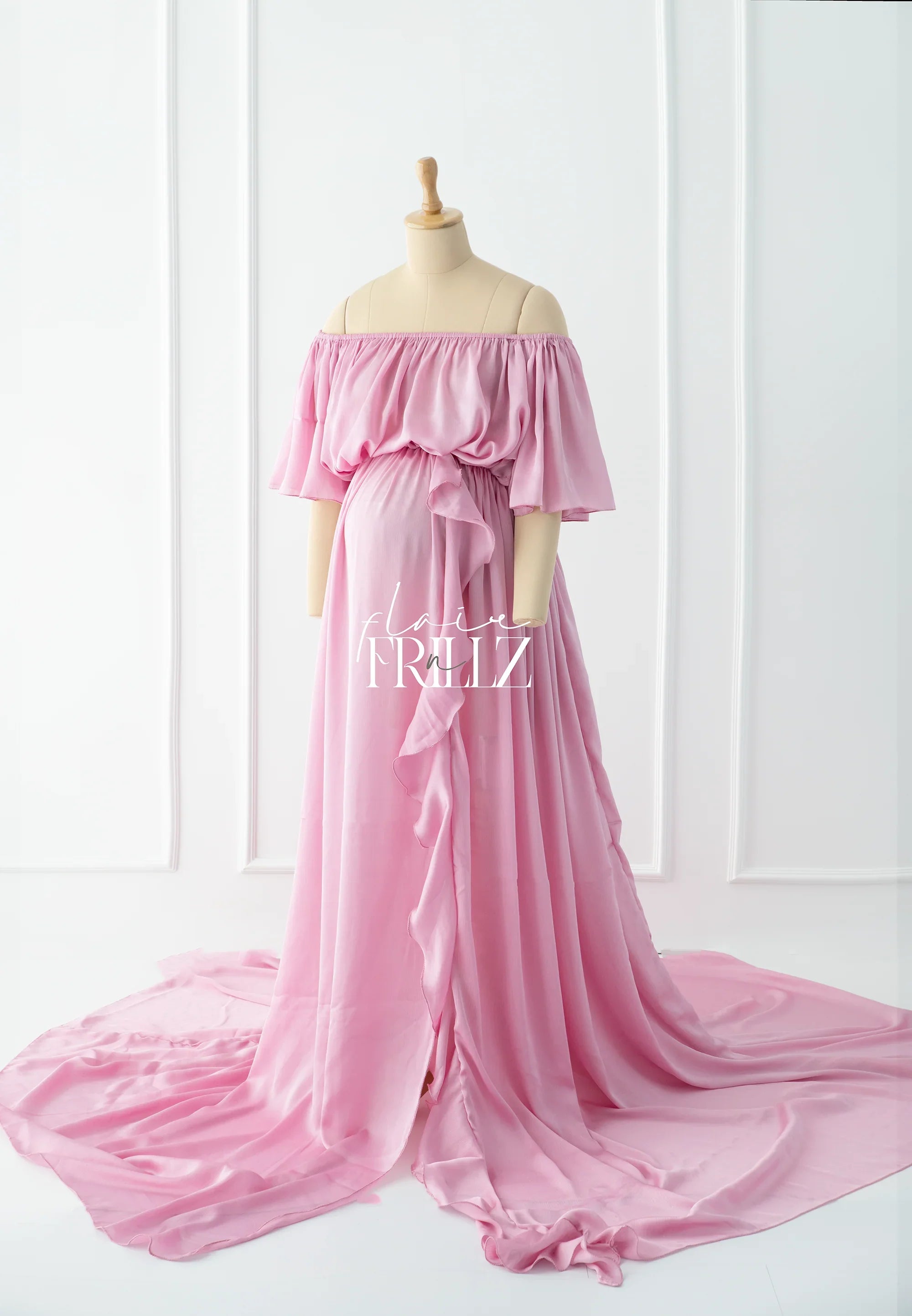 Pink off-shoulder ruffle maternity gown with flowing train on mannequin in studio