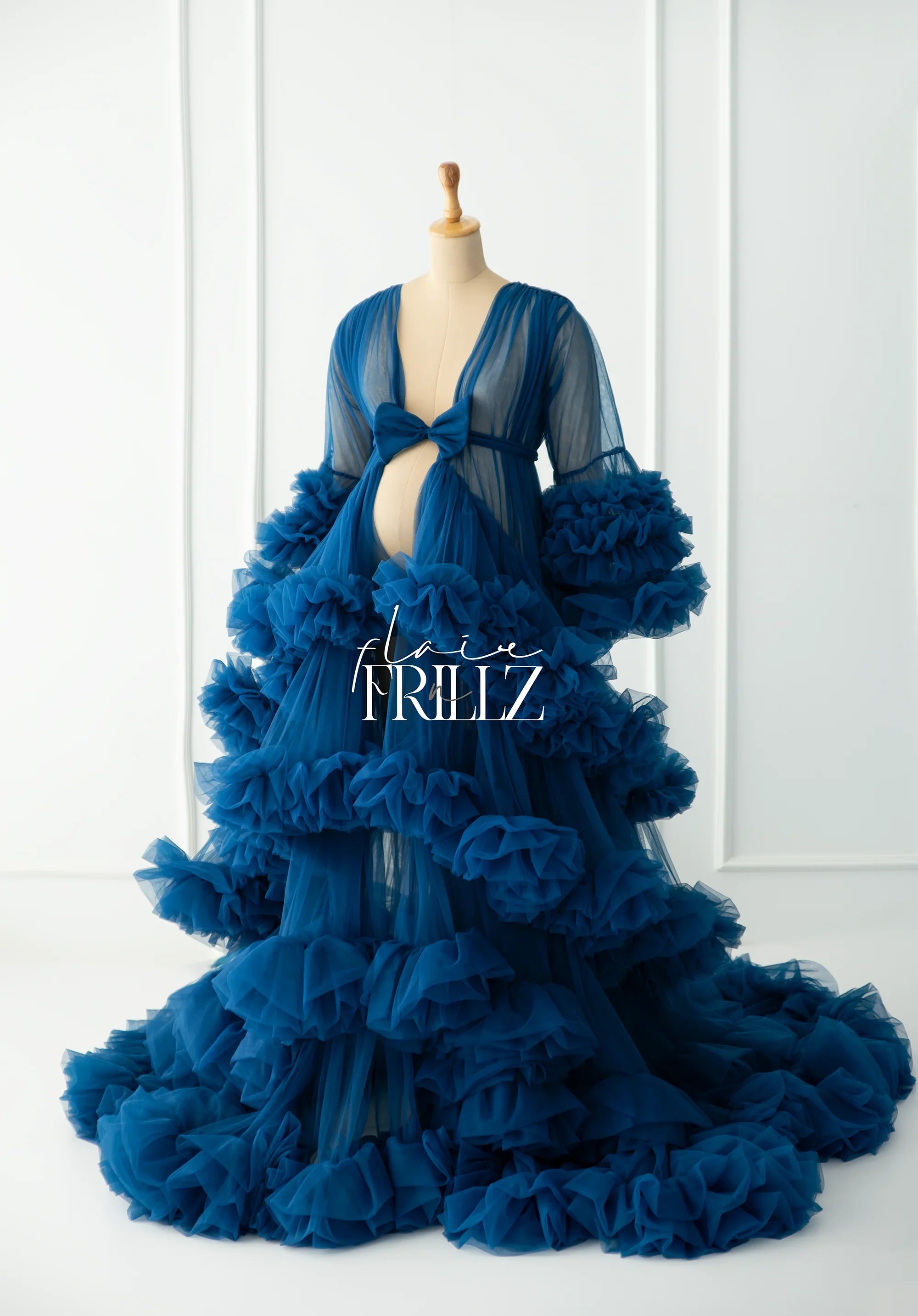 Blue ruffled maternity gown with sheer fabric and bow detail on a dress form.