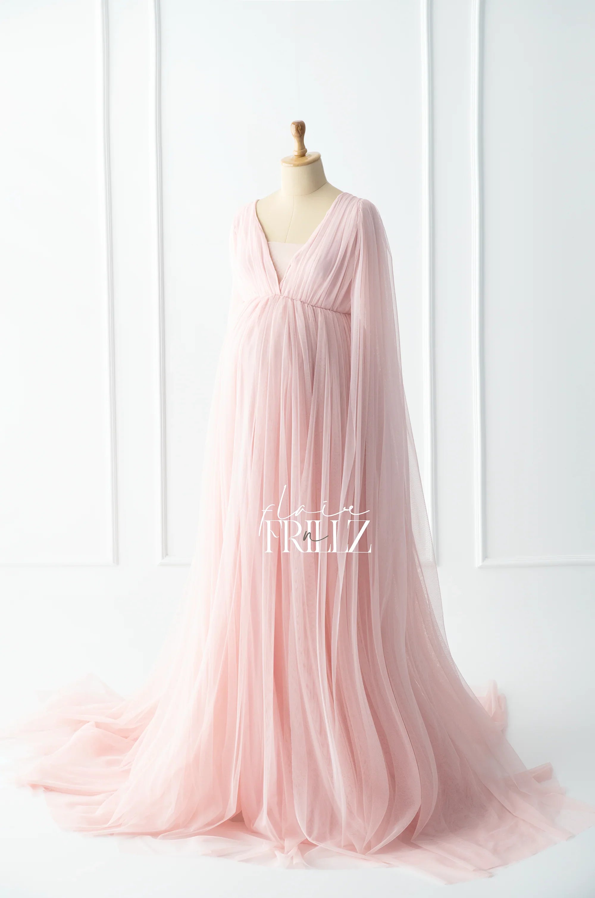 Long blush pink maternity gown with sheer tulle overlay and flowing sleeves on mannequin