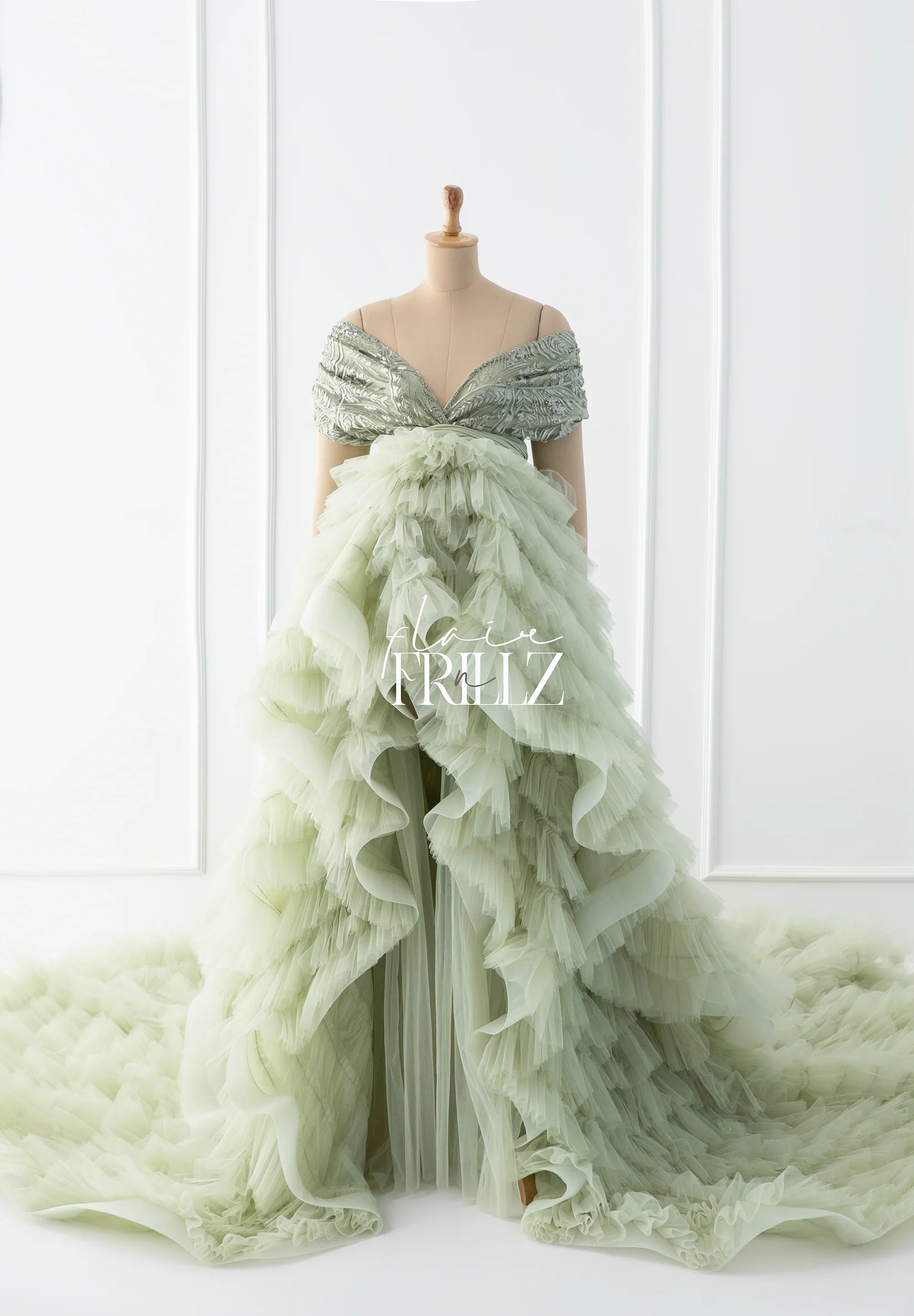 Sage green off-shoulder maternity gown with layered tulle skirt and ruffled train on mannequin