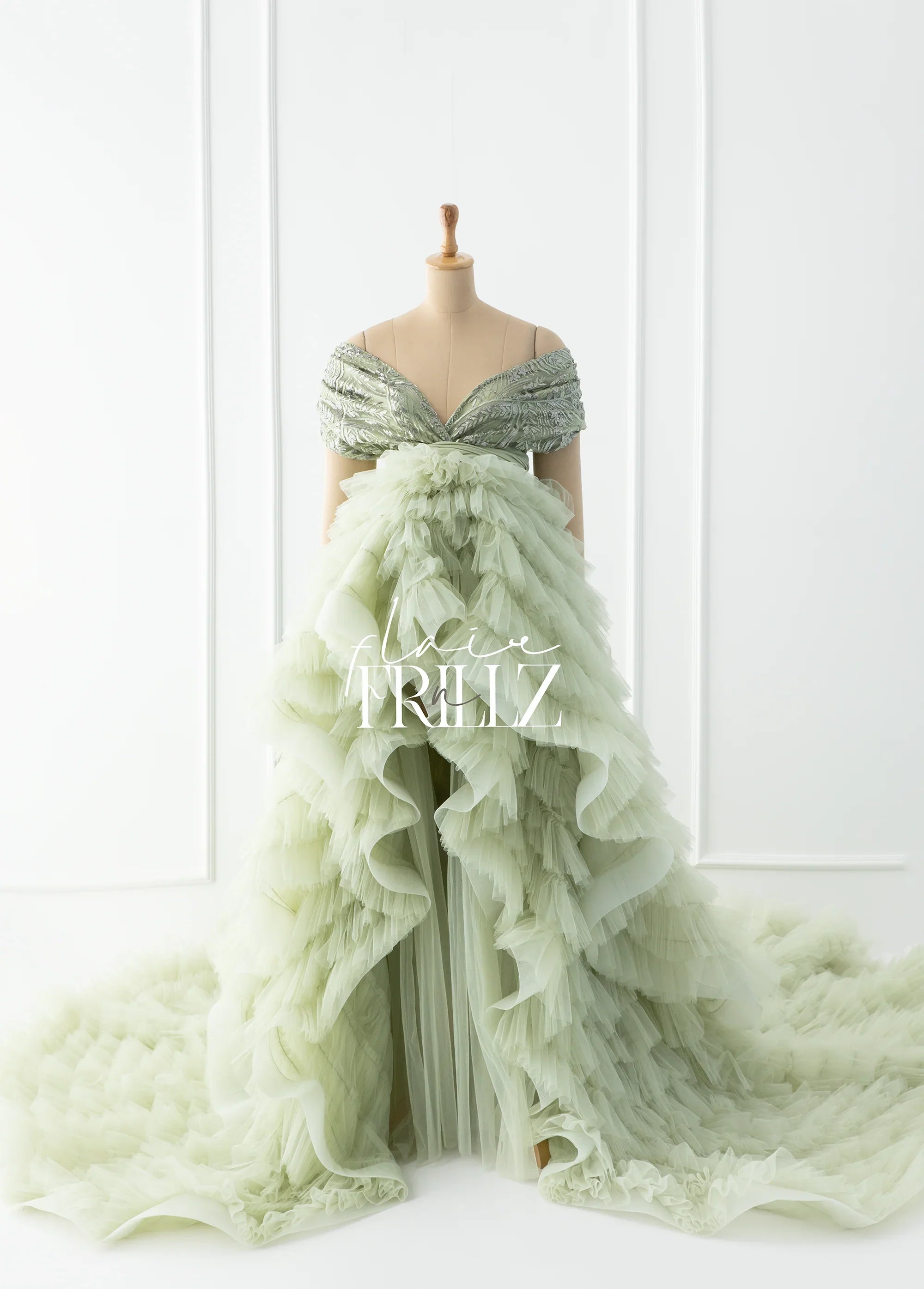 Mint green off-shoulder ruffled maternity gown with layered tulle train on mannequin.