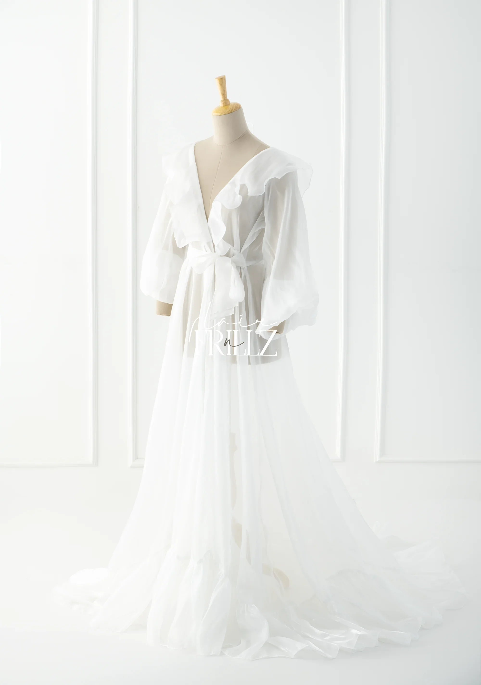 Sheer white maternity gown with ruffled sleeves, deep V-neck, and flowing train on mannequin
