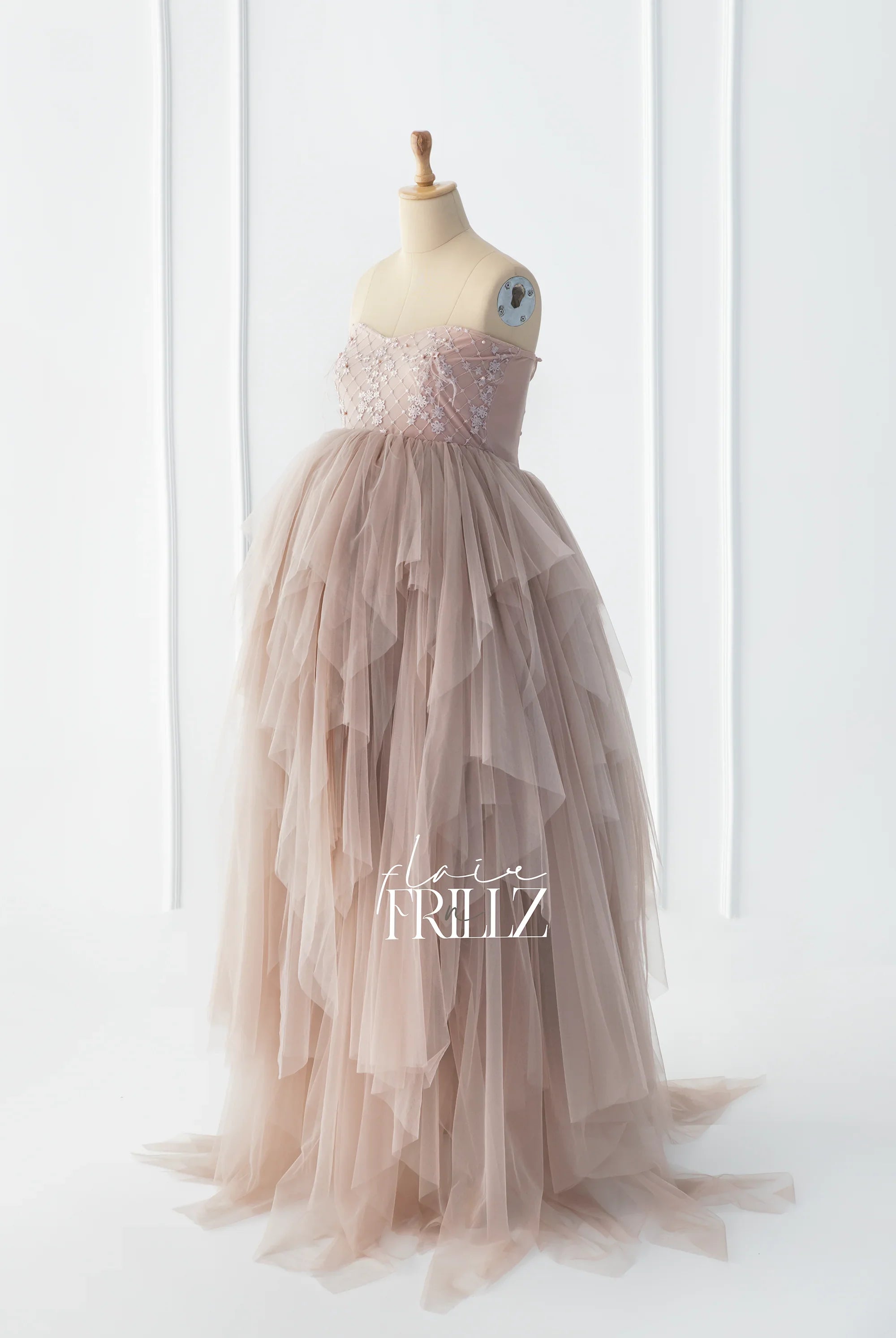Blush pink tulle maternity gown with layered ruffles and floral embroidery on a dress form