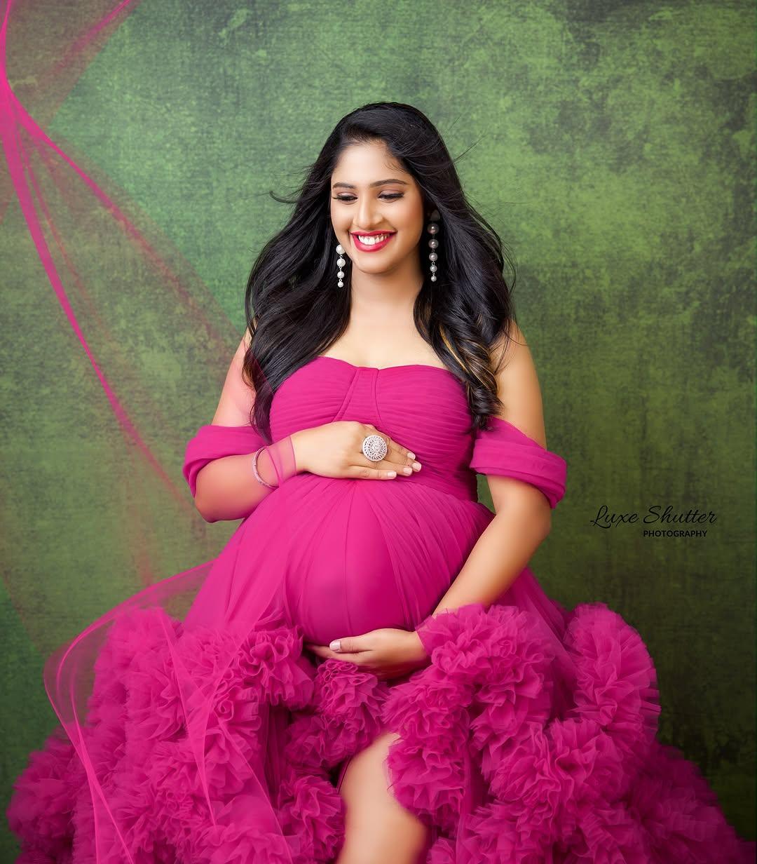 Smiling pregnant woman in a ruffled magenta maternity gown against a green backdrop