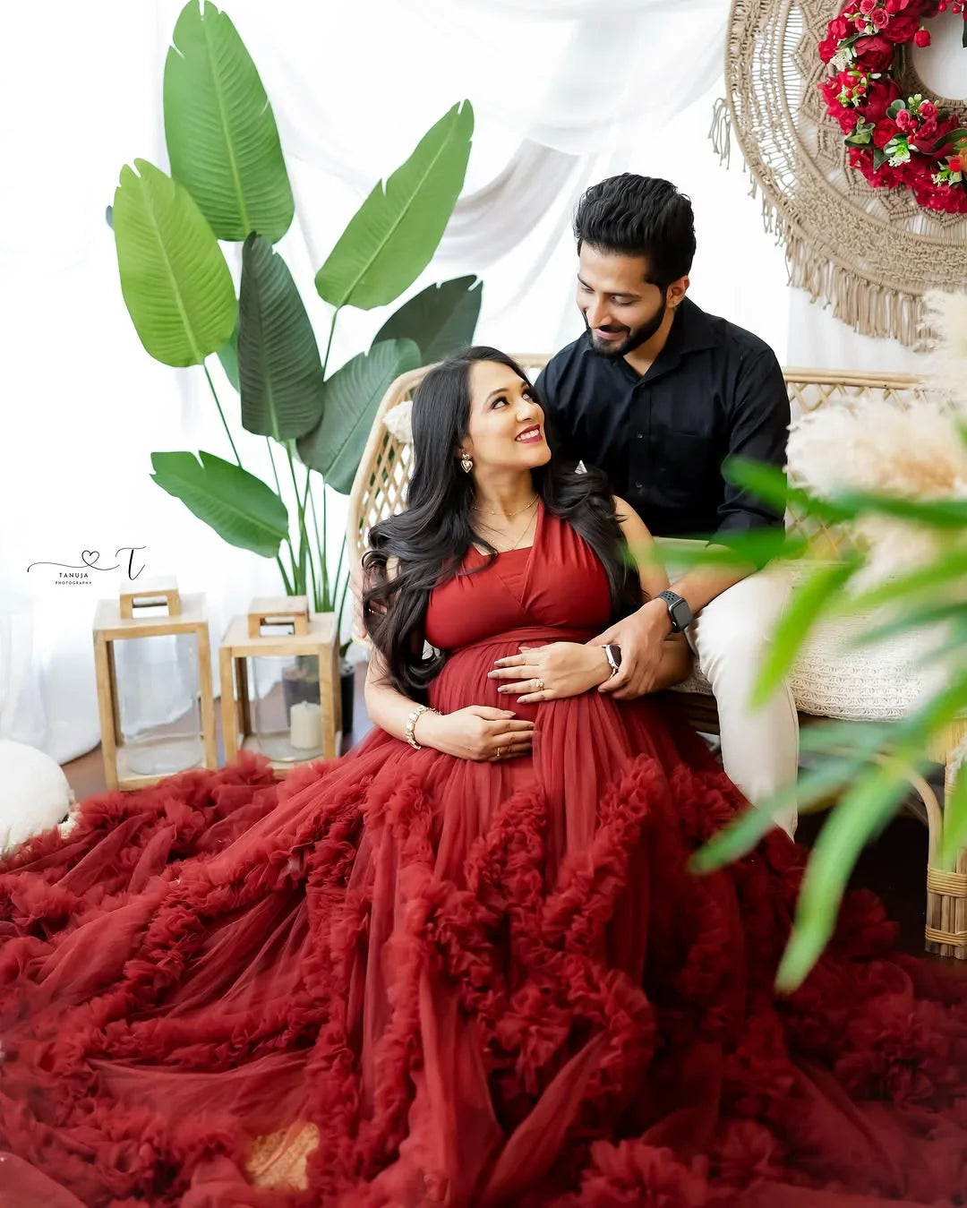 Smiling pregnant woman in elegant red maternity gown sits with partner in cozy, stylish room