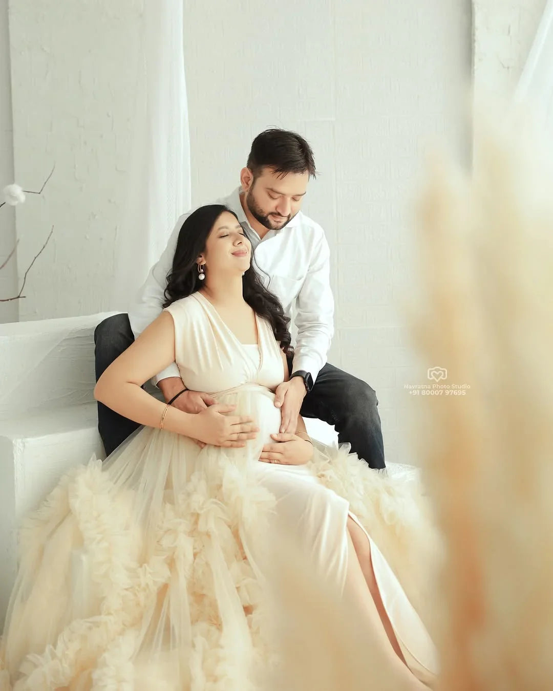 Pregnant woman in elegant cream maternity gown with partner, soft natural light, serene setting